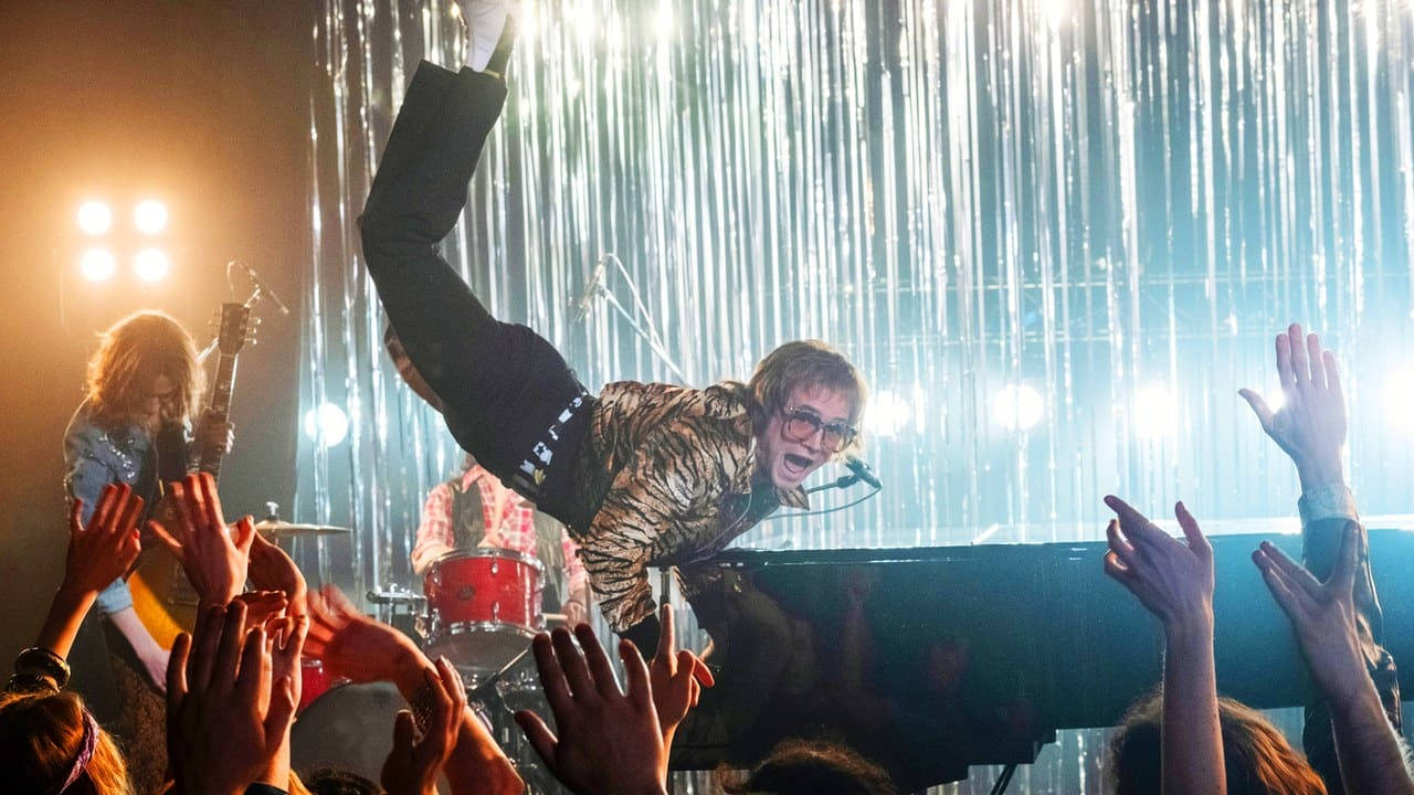 Rocketman 群眾中飛翔 壁紙 — 一位穿著虎紋外套的表演者凌空躍過觀眾，舞台燈光穿過他們背後的銀色窗簾照射出來。