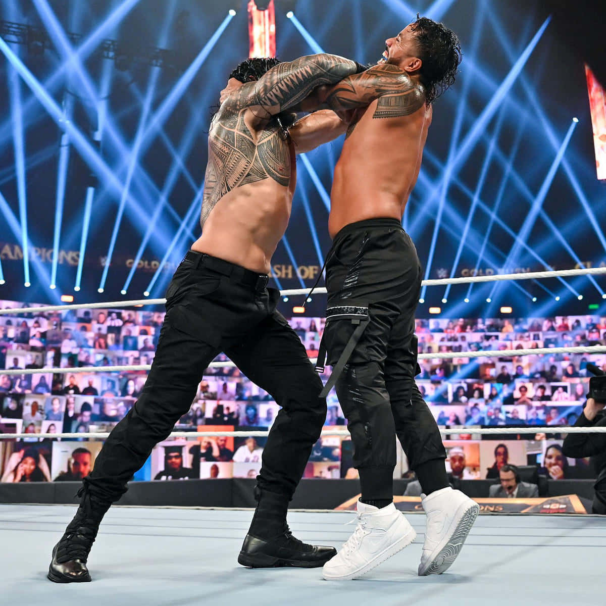 Roman Reigns 對決 Jey Uso 壁紙 — 兩名肌肉發達的摔角手在明亮的藍色舞台燈光下於擂台上激烈纏鬥，背景中可見一群粉絲。