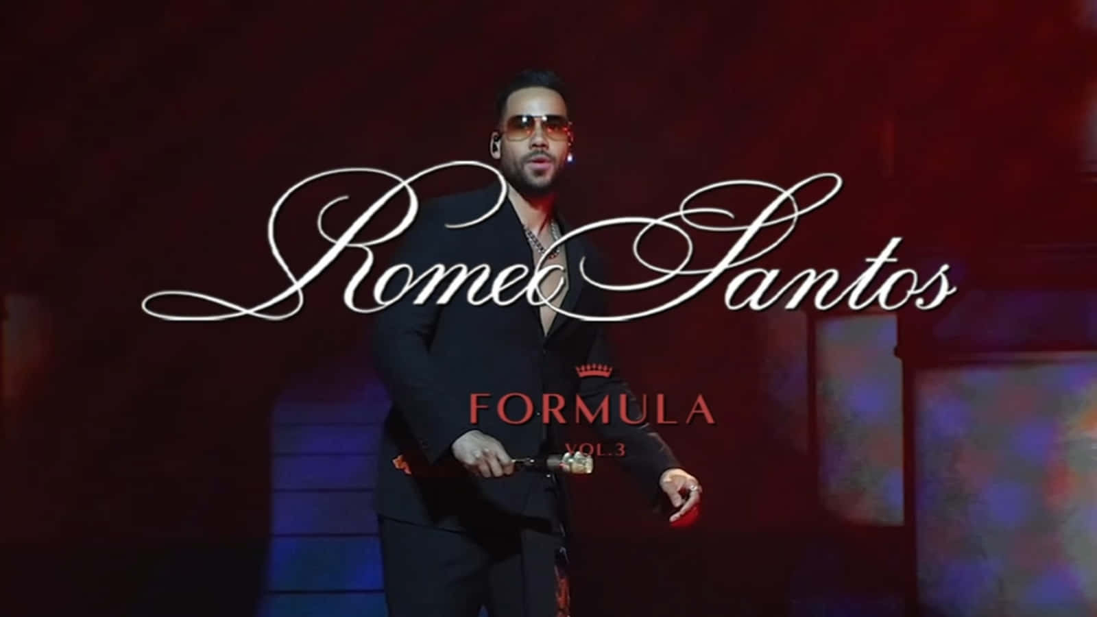  壁紙 — Romeo Santos 自信地穿著黑色西裝，在戲劇性的紅色燈光下，帶有優雅的白色草書文字疊加。