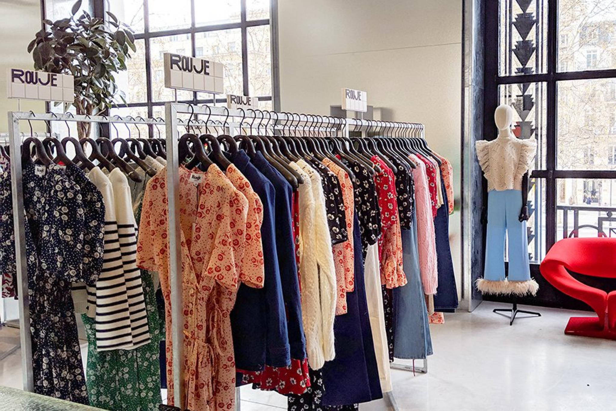 Rouje 店內連衣裙陳列 壁紙 — 一間時尚精品店在大型窗戶附近展示色彩繽紛的連衣裙，配有模特兒和紅色椅子。