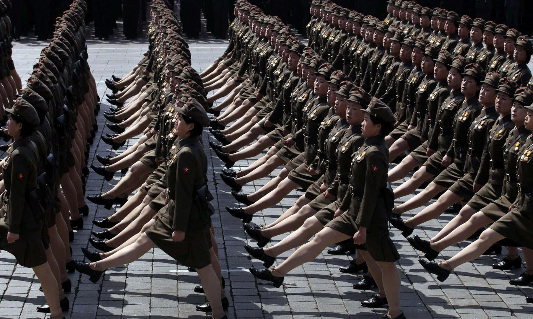 North Korea 桌布 壁紙 — 一排排身穿制服的女兵在明亮的日光下，在鋪砌的廣場上以完美同步的隊形行進。