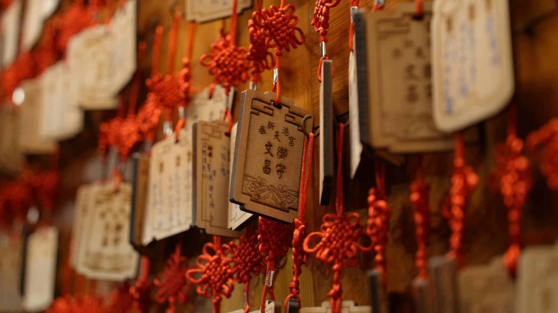  壁紙 — 一排排帶有中文字的木製祈福牌掛在鮮紅色的中國結上，襯著溫暖的木牆。