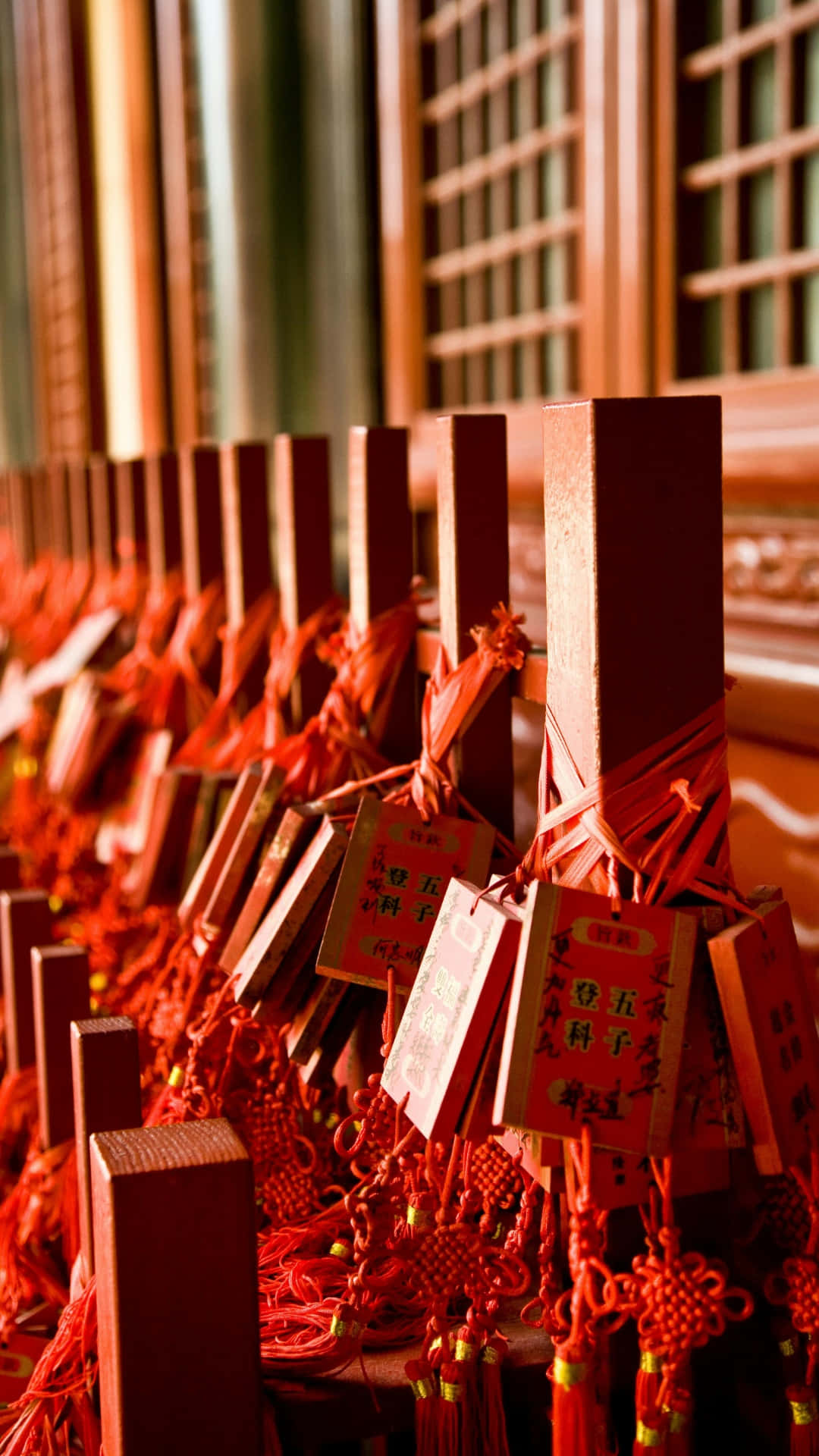  壁紙 — 一排排裝飾著紅色絲帶和漢字的木製祈願棒，在傳統格子窗附近的溫暖陽光中矗立。
