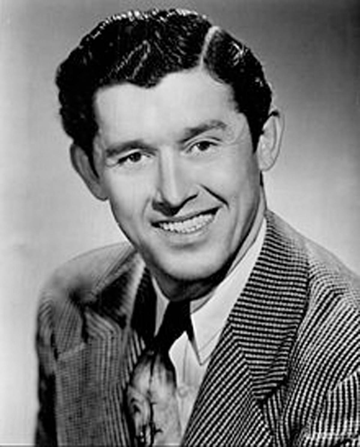 Roy Acuff 微笑 黑白肖像 壁紙 — 一位微笑的男士穿著細條紋西裝和領帶，為經典黑白工作室肖像擺姿勢。