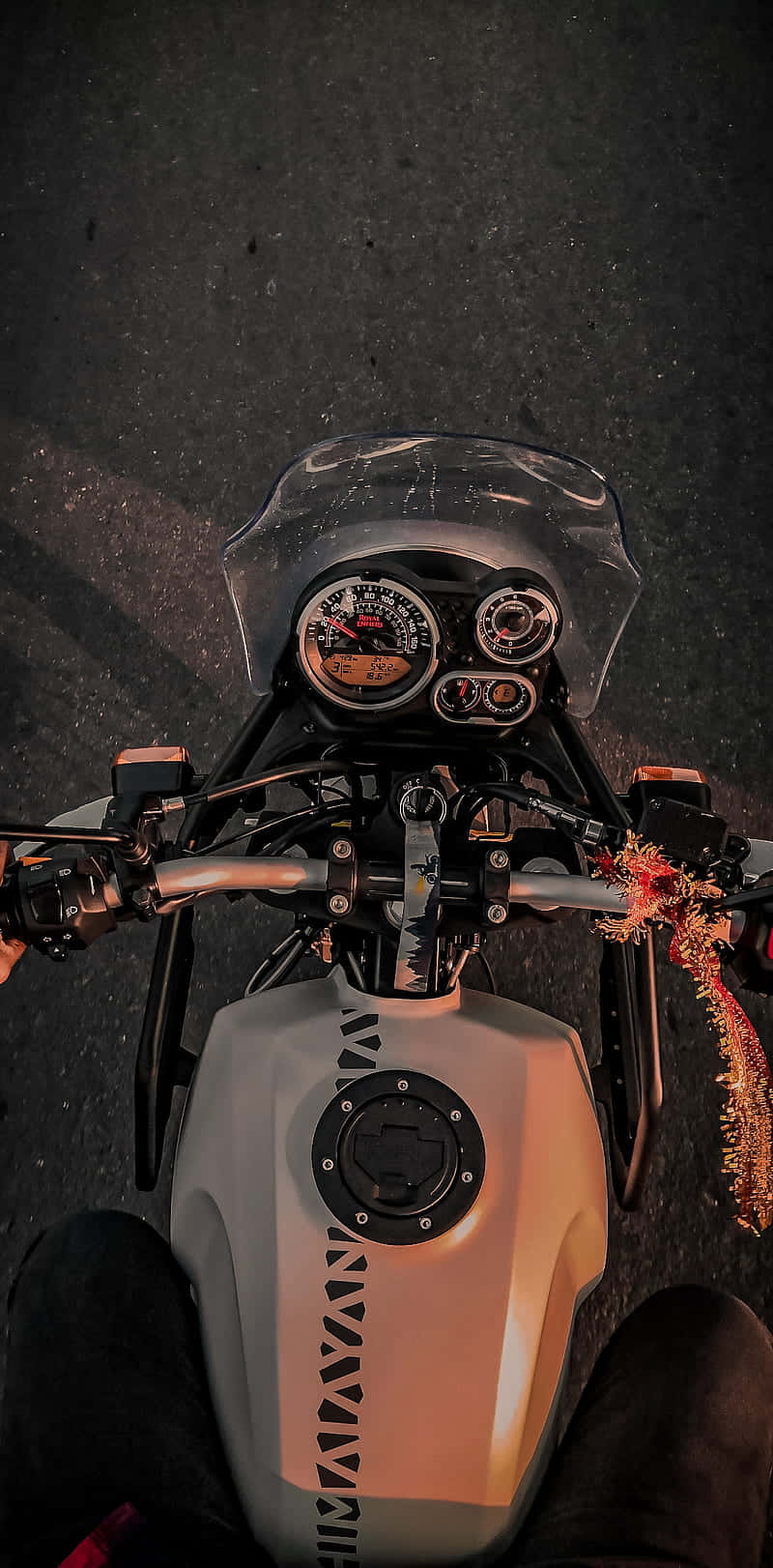 白色 Royal Enfield Himalayan 頂視圖 iPhone 壁紙 — 夜晚從銀色電單車上方以第一人稱視角觀看，發光錶盤和把手上的節日花環。