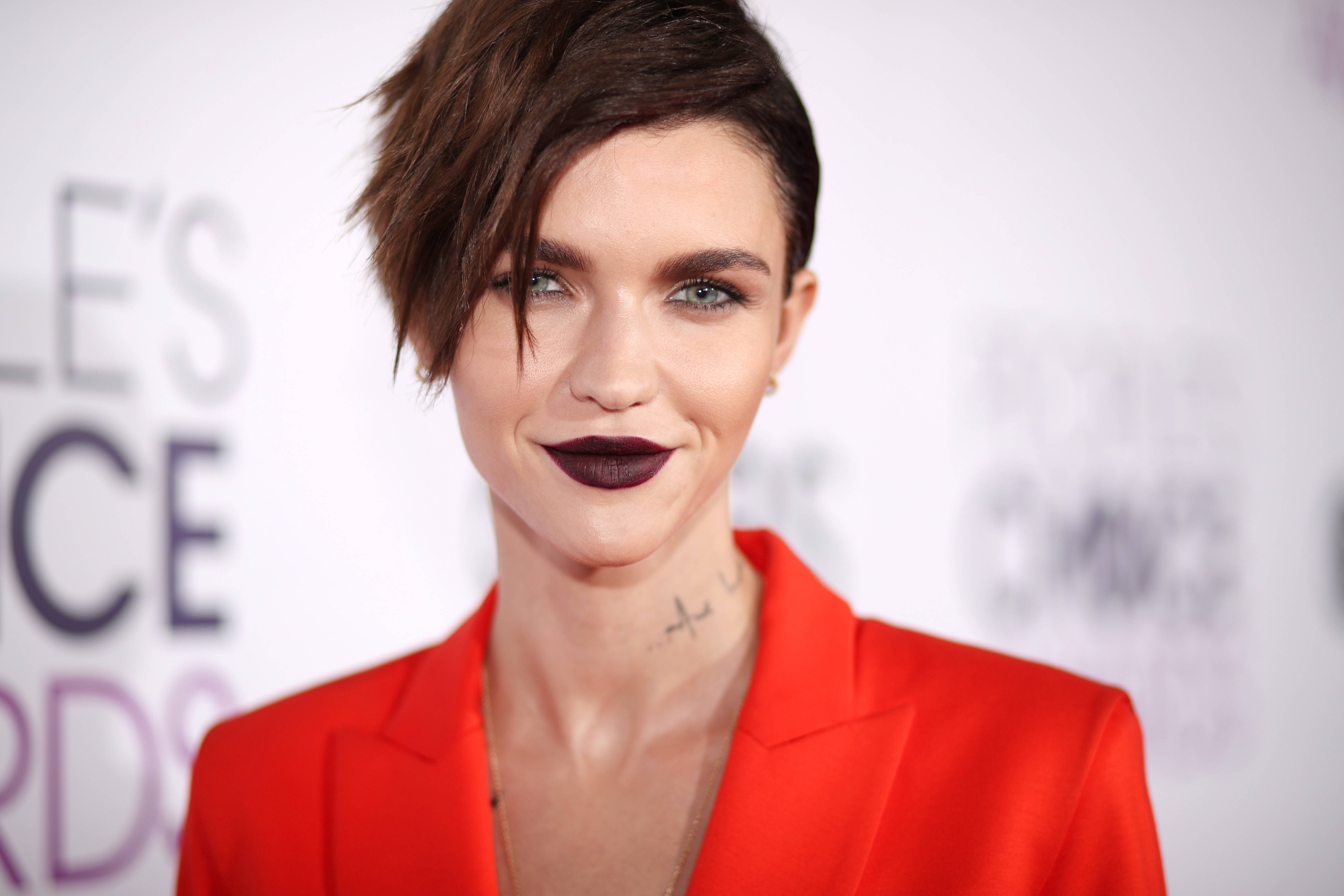 Ruby Rose 2017 人民選擇獎 壁紙 — 一位短黑髮、塗著大膽深色唇膏的女性，在頒獎典禮上穿著鮮紅色西裝外套微笑。