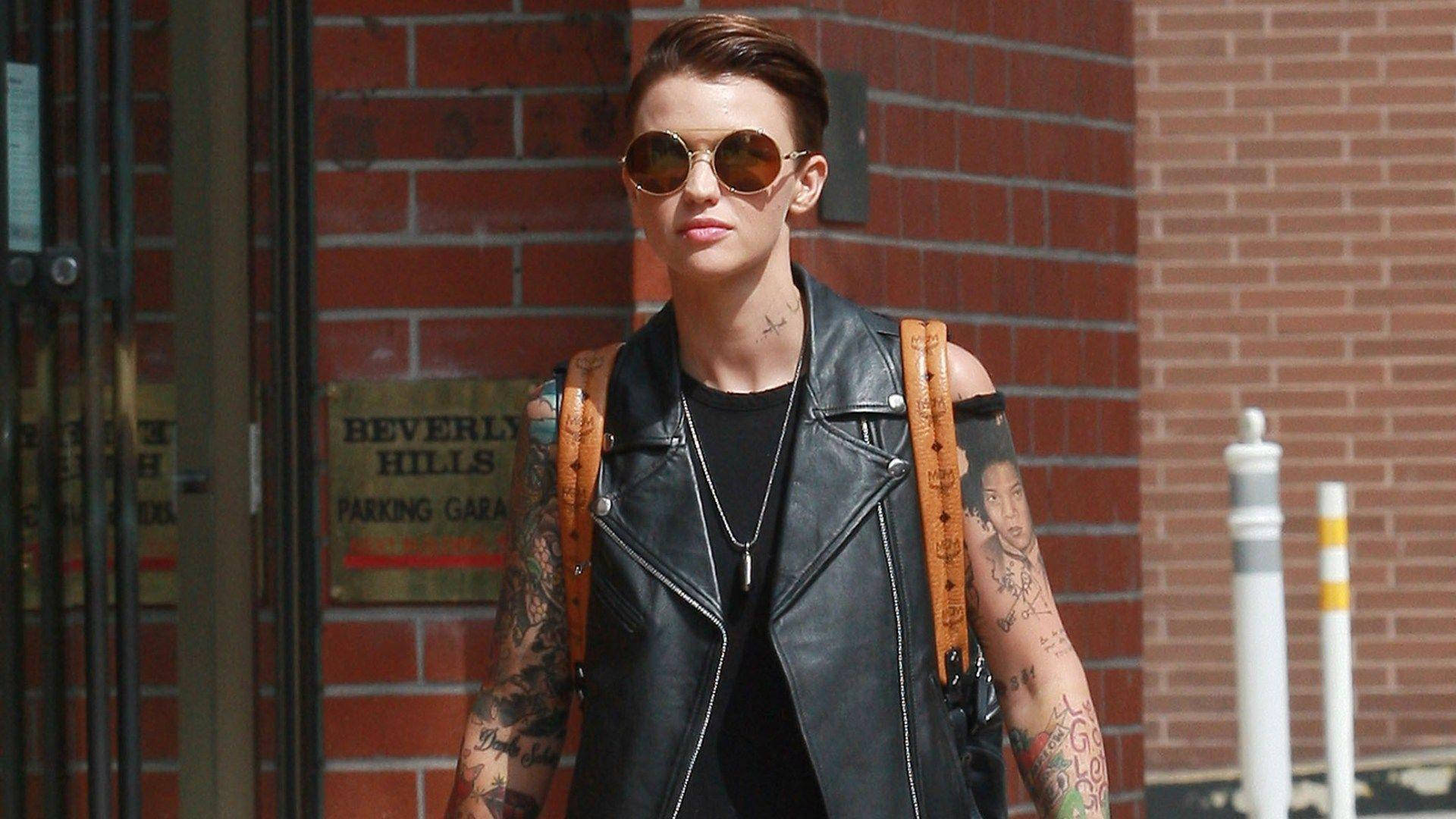 Ruby Rose 休閒造型 壁紙 — 一位紋身女子穿著黑色皮背心和圓形太陽眼鏡，自信地走過比華利山停車場標誌。