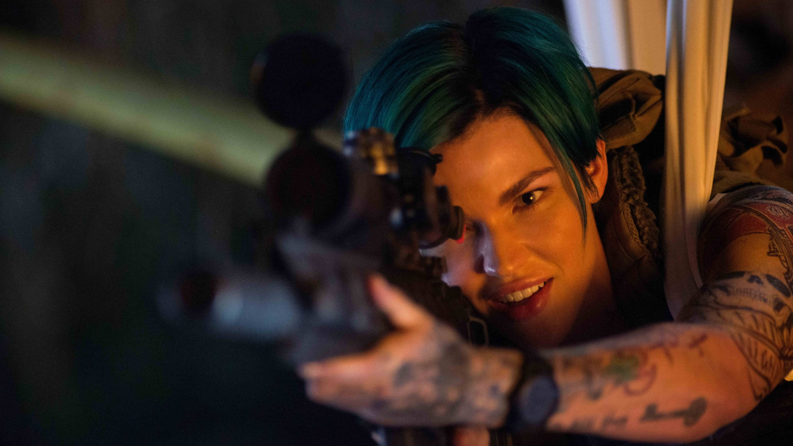 Ruby Rose 精準狙擊手造型 壁紙 — 一個擁有青綠色頭髮和紋身的人，在昏暗的環境中專注地瞄準步槍。