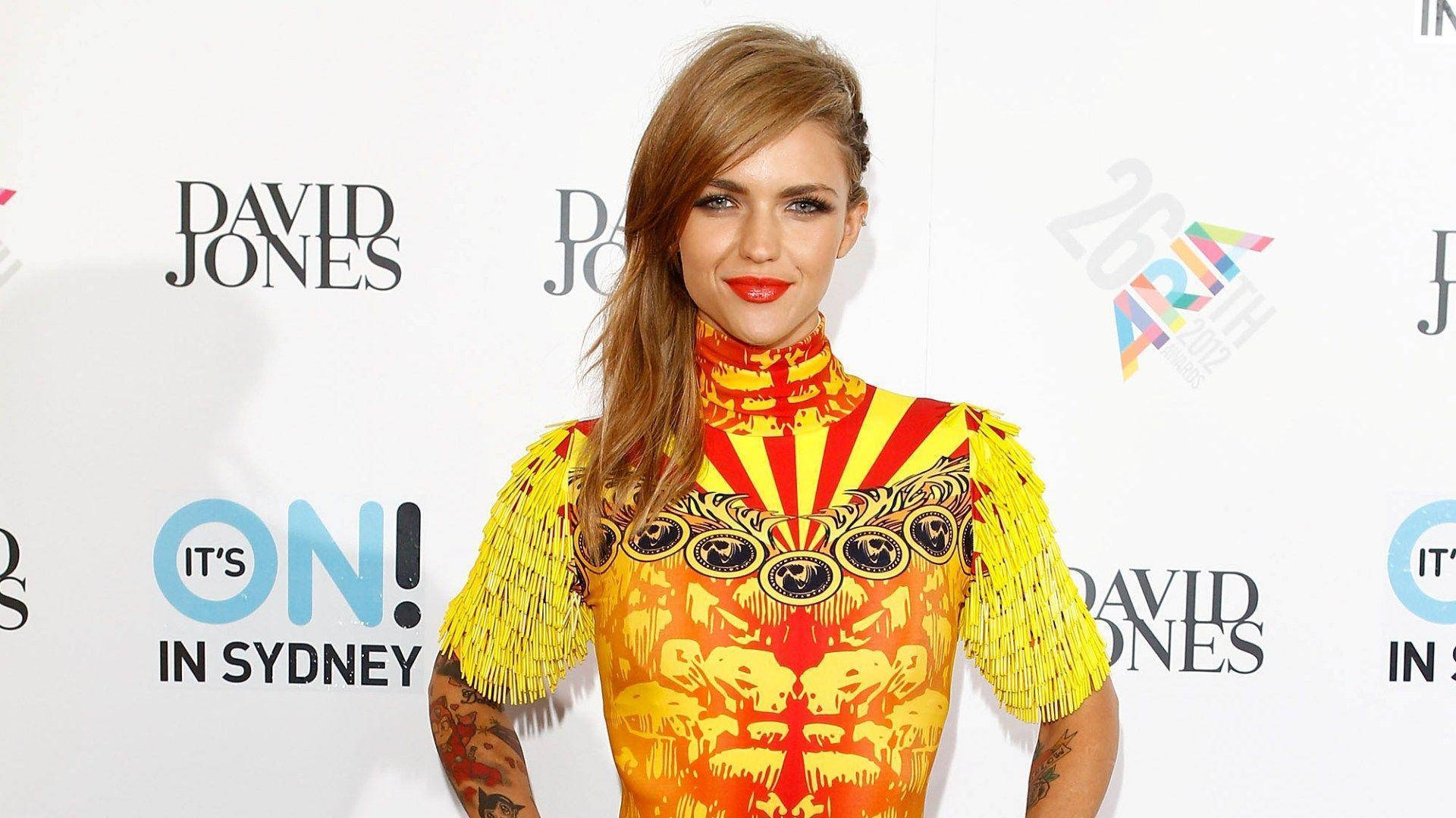Ruby Rose 長金髮造型 壁紙 — 一位身穿鮮豔黃橙色圖案連衣裙、帶有流蘇袖子的女士在悉尼活動中自信地擺姿勢。