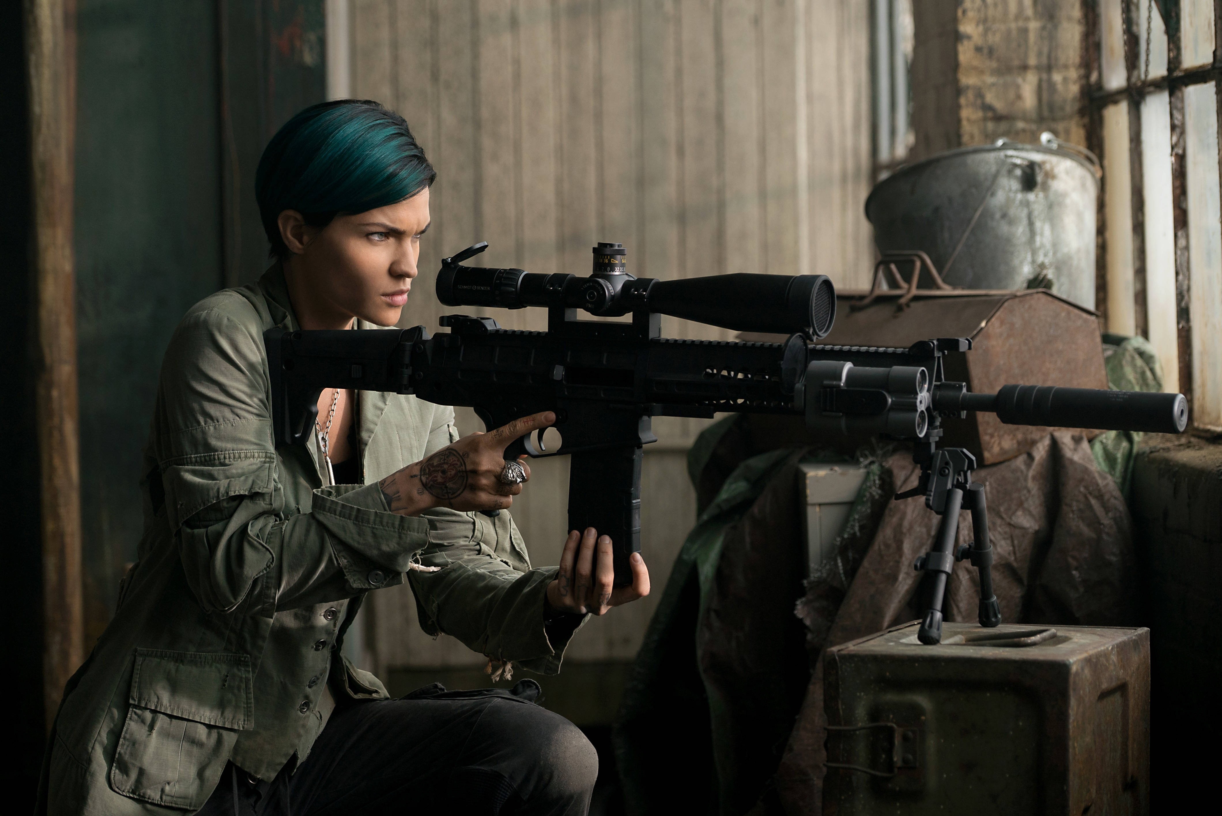 Ruby Rose 飾演 Adele Wolff 壁紙 — 一位擁有藍綠色頭髮的女性蹲在骯髒的房間裡，專注地瞄準帶瞄準鏡的步槍。