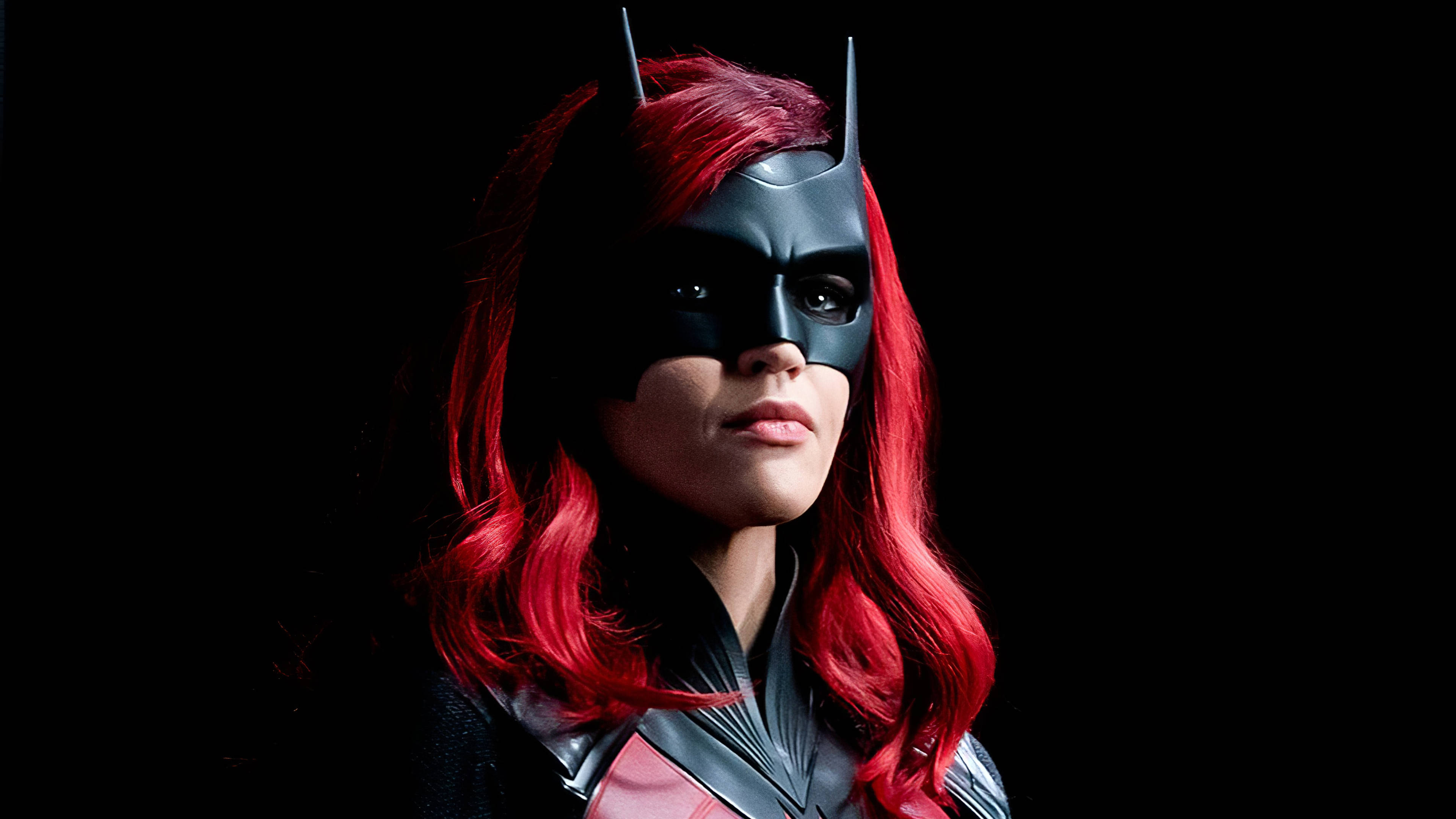 Ruby Rose 飾演 Batwoman 壁紙 — 一位紅髮的兇猛蝙蝠女俠，身穿黑色頭罩和緊身衣，在純黑背景下凝視前方。