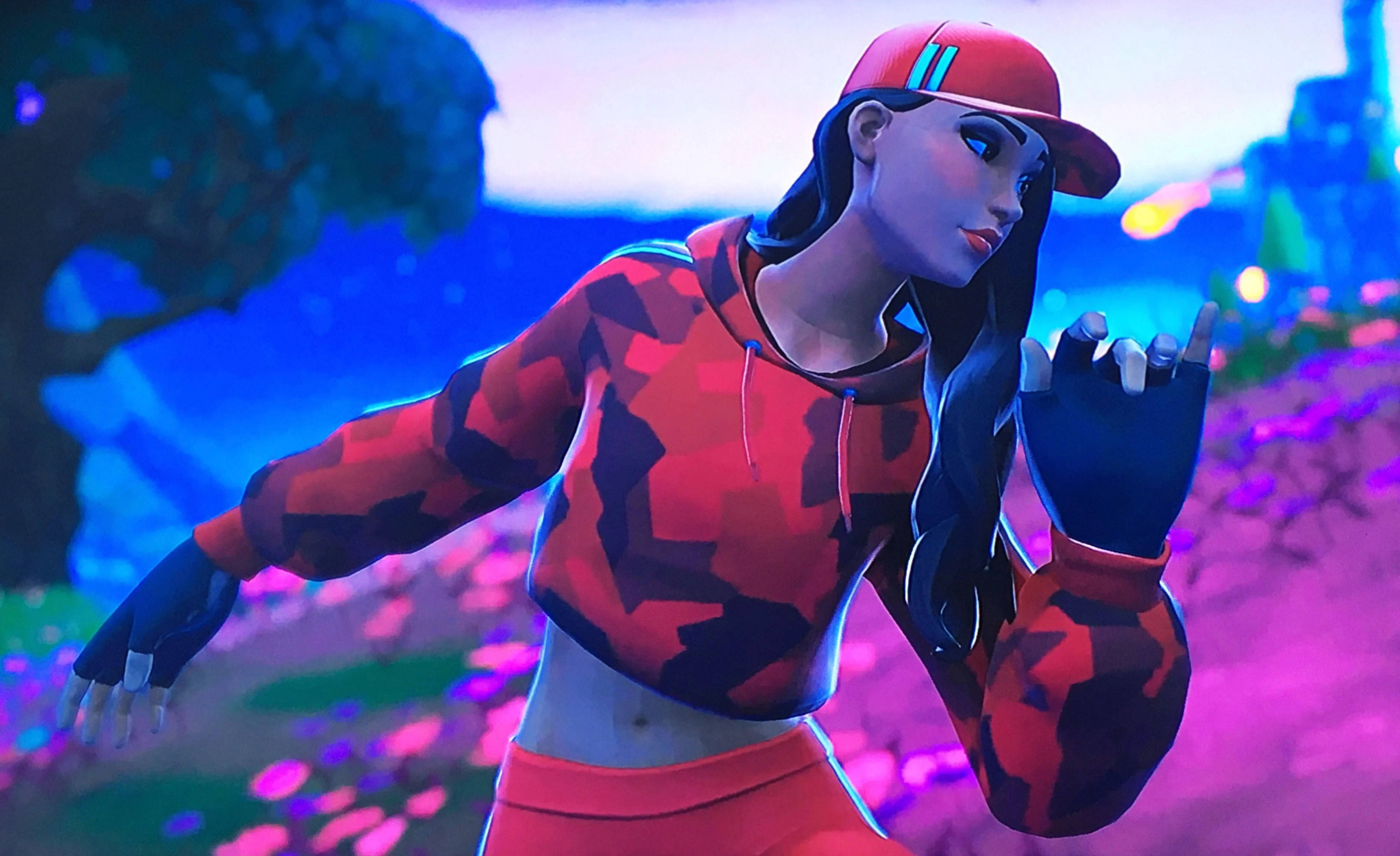 Ruby《Fortnite》側面遊戲姿勢 壁紙 — 一個風格化的女性角色穿著紅色迷彩連帽衫和帽子，在暮色天空下發光的紫色花朵中擺姿勢。