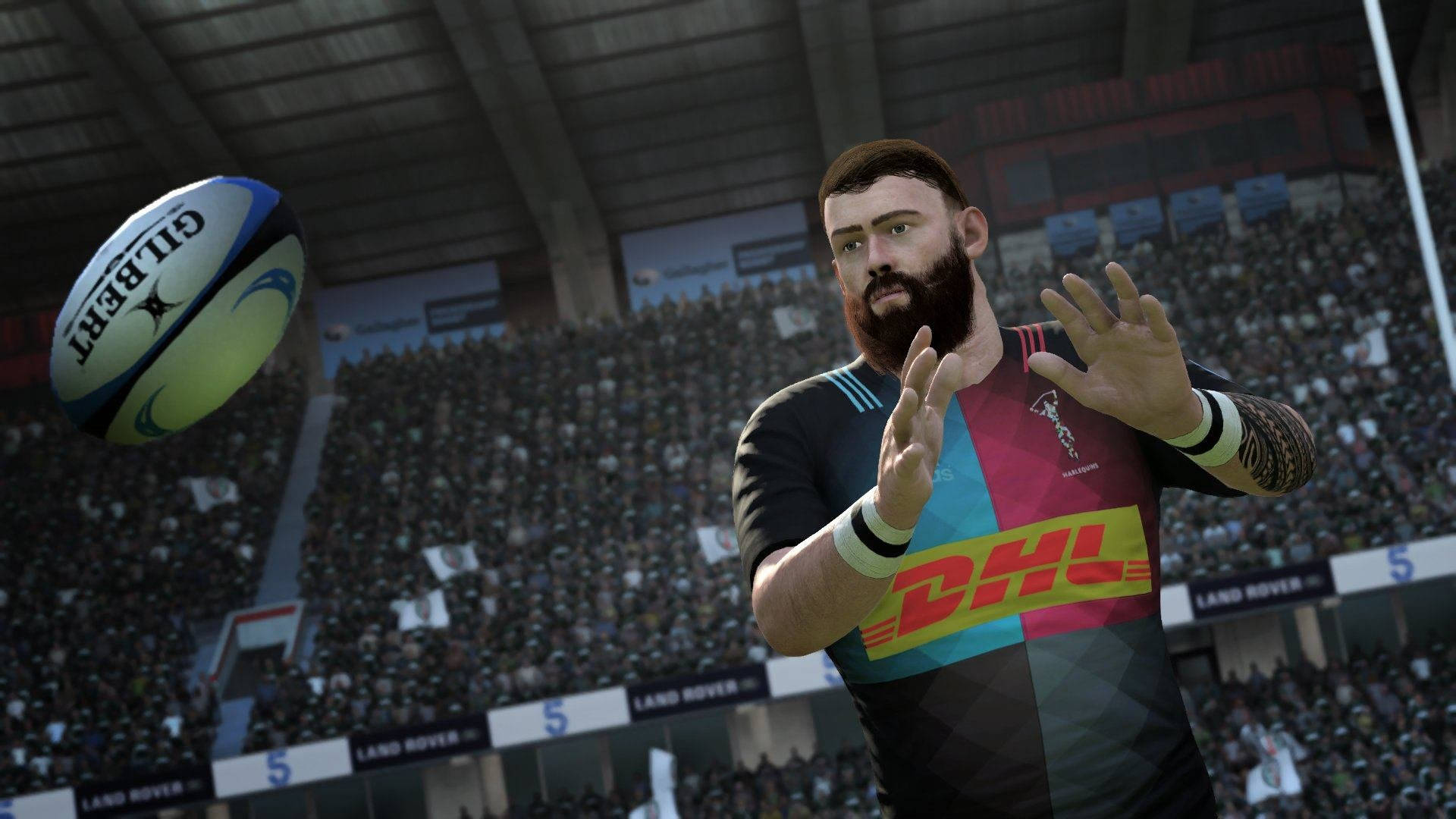 《Rugby 22》遊戲畫面 壁紙 — 一名穿著彩色球衣的欖球運動員在明亮的燈光下，於座無虛席的體育場準備接住Gilbert球。