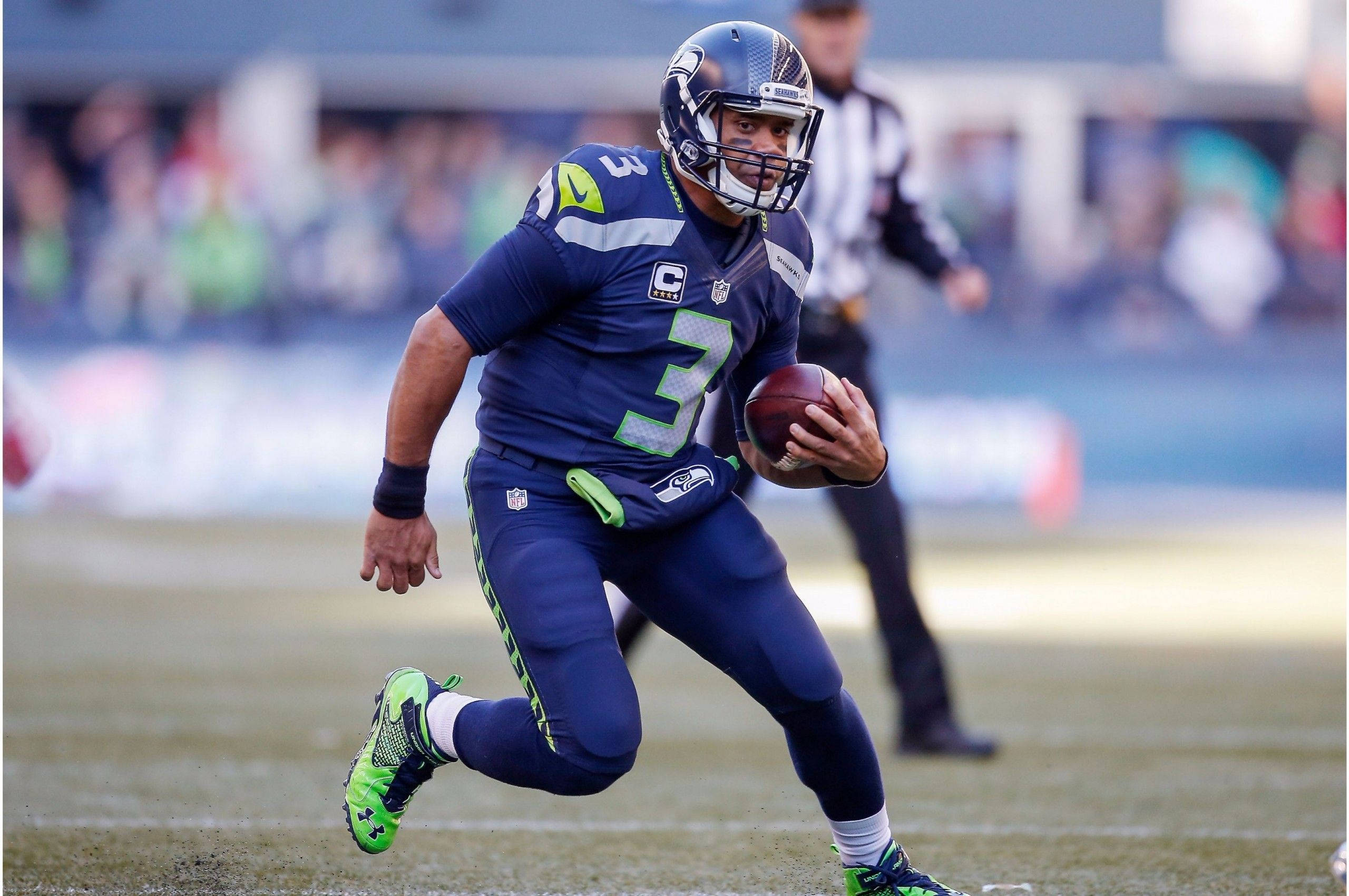 Russell Wilson 跑步跳躍 壁紙 — 西雅圖海鷹隊四分衛羅素·威爾遜身穿藍綠球衣，在日間比賽中持球奔跑。