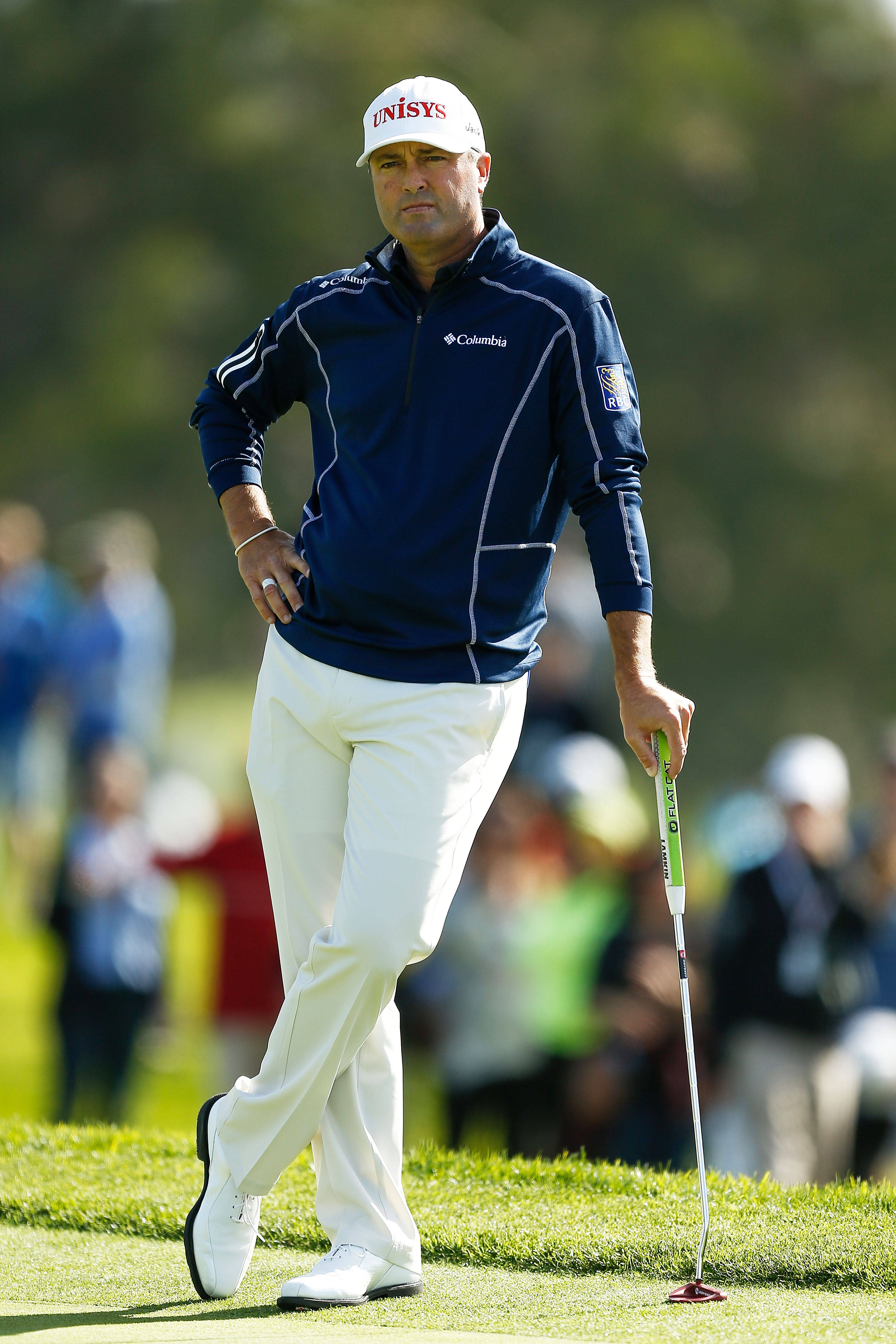 Ryan Palmer 靠著高爾夫球桿 壁紙 — 一位專注的高爾夫球手身穿海軍藍和白色裝備，在陽光明媚的綠色高爾夫球場上拿著推桿行走。