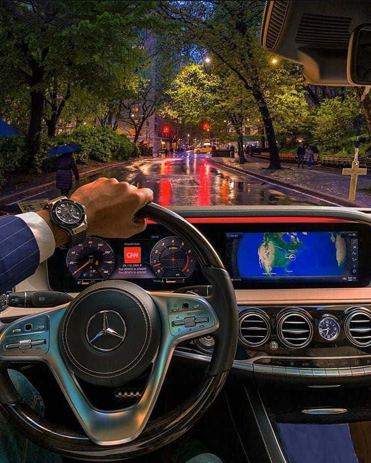 梅賽德斯-奔馳S級車內 壁紙 — 司機的手在夜間握著豪華車的方向盤，潮濕的城市街道反射著紅綠燈和路邊的綠樹。