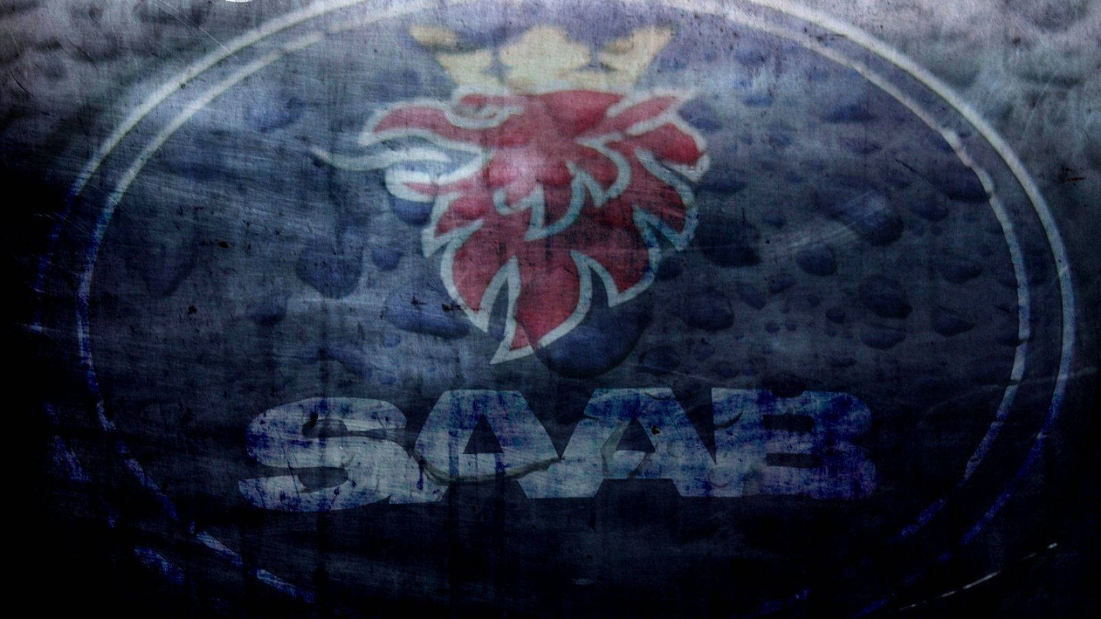 Saab 標誌 壁紙 — 一個磨損的SAAB標誌，帶有紅色皇冠獅子徽章，位於深色紋理表面上。