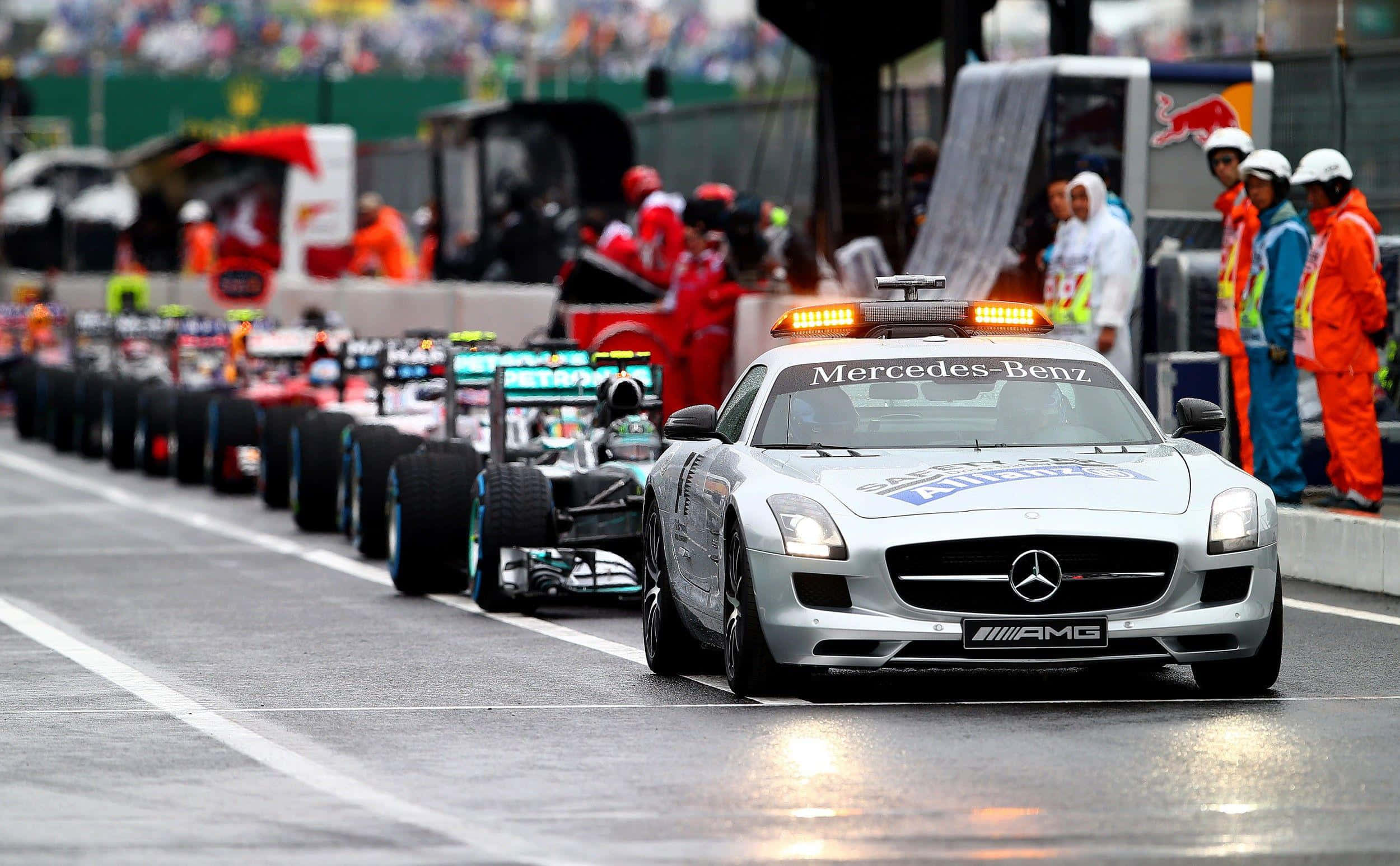 高性能Safety Car馳騁賽道 壁紙 — 一架銀色 Mercedes-Benz 安全車帶領一排 Formula 1 賽車在濕滑賽道上行駛，附近有身穿橙色套裝的工作人員。