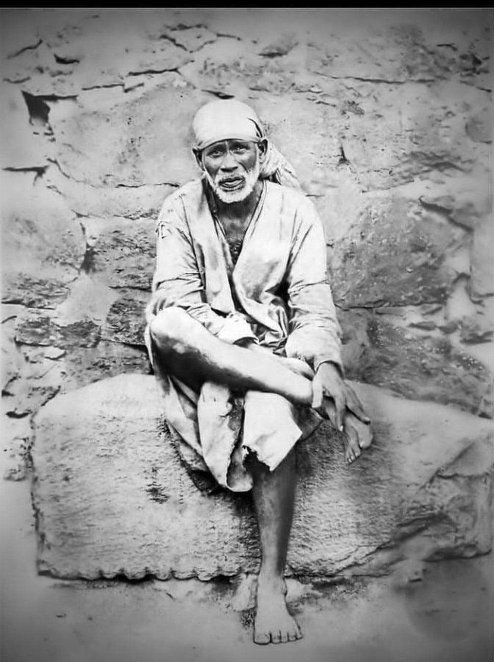 復古黑白照片 Sai Baba 手機壁紙 壁紙 — 一位留著白鬍子的老人赤腳坐在石階上，背景是粗糙紋理的牆壁，復古黑白照片。