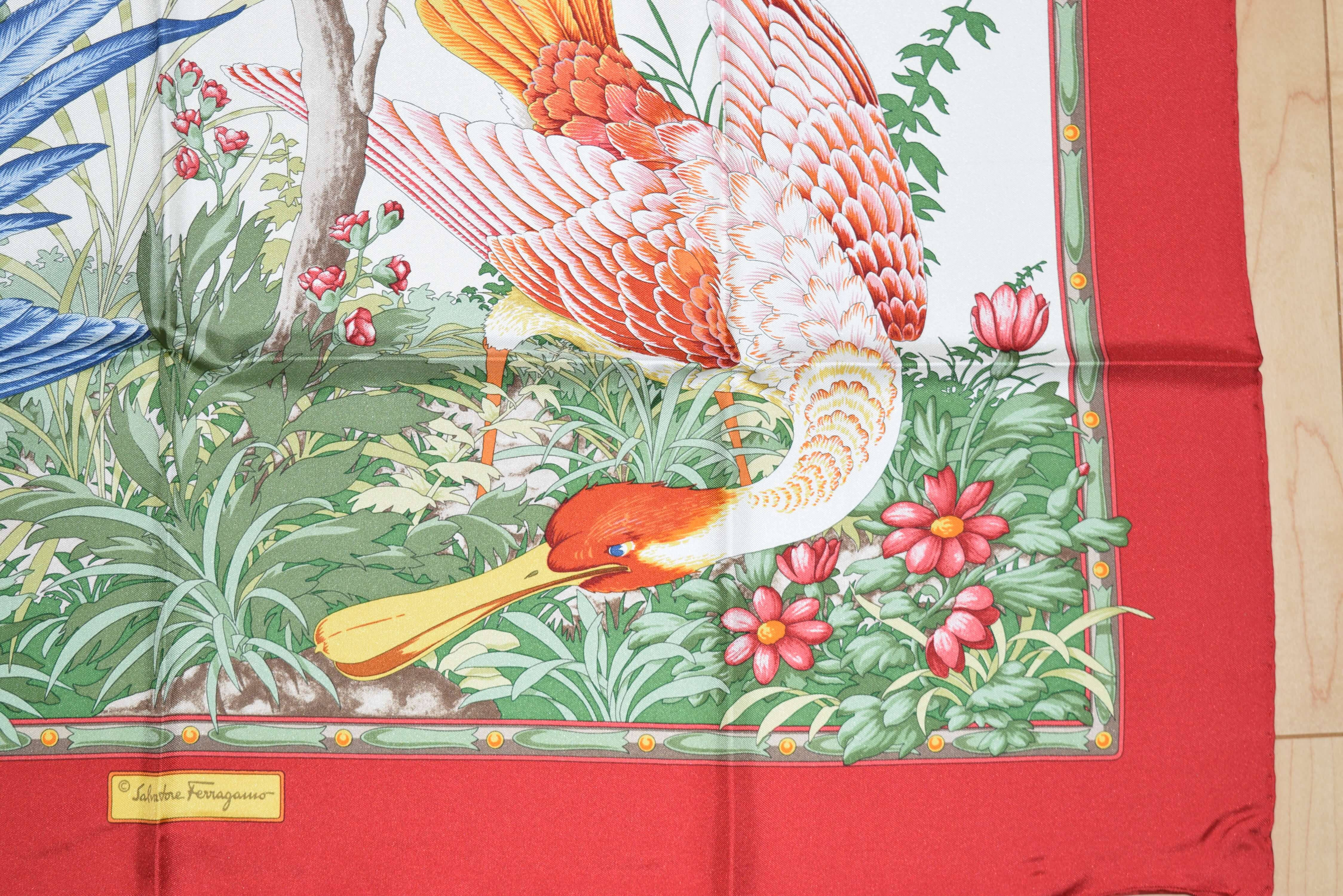 Salvatore Ferragamo 鳥紋布料 壁紙 — 一條充滿活力的絲巾上，有粉紅色和白色鳥類的精細插圖，周圍環繞著茂密的綠色葉子和粉紅色花朵，並帶有醒目的紅色邊框。