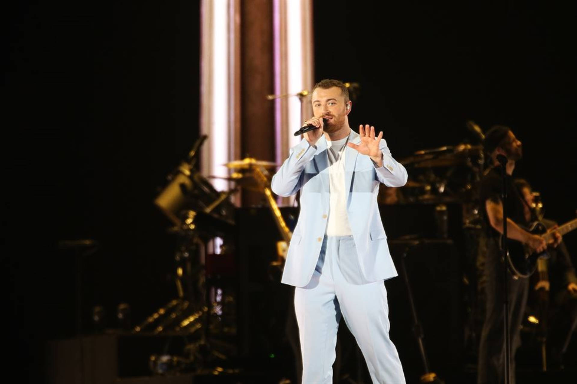 身穿淺藍色西裝的男歌手在舞台上與樂隊演出