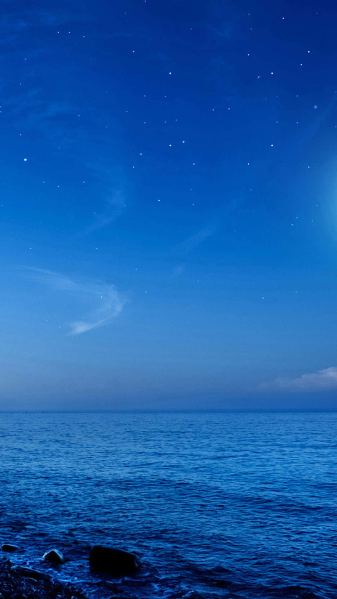 體驗革命性的 Samsung Galaxy 壁紙 — 寧靜的夜晚場景，深藍色星空下平靜的海洋與岩石海岸相接。