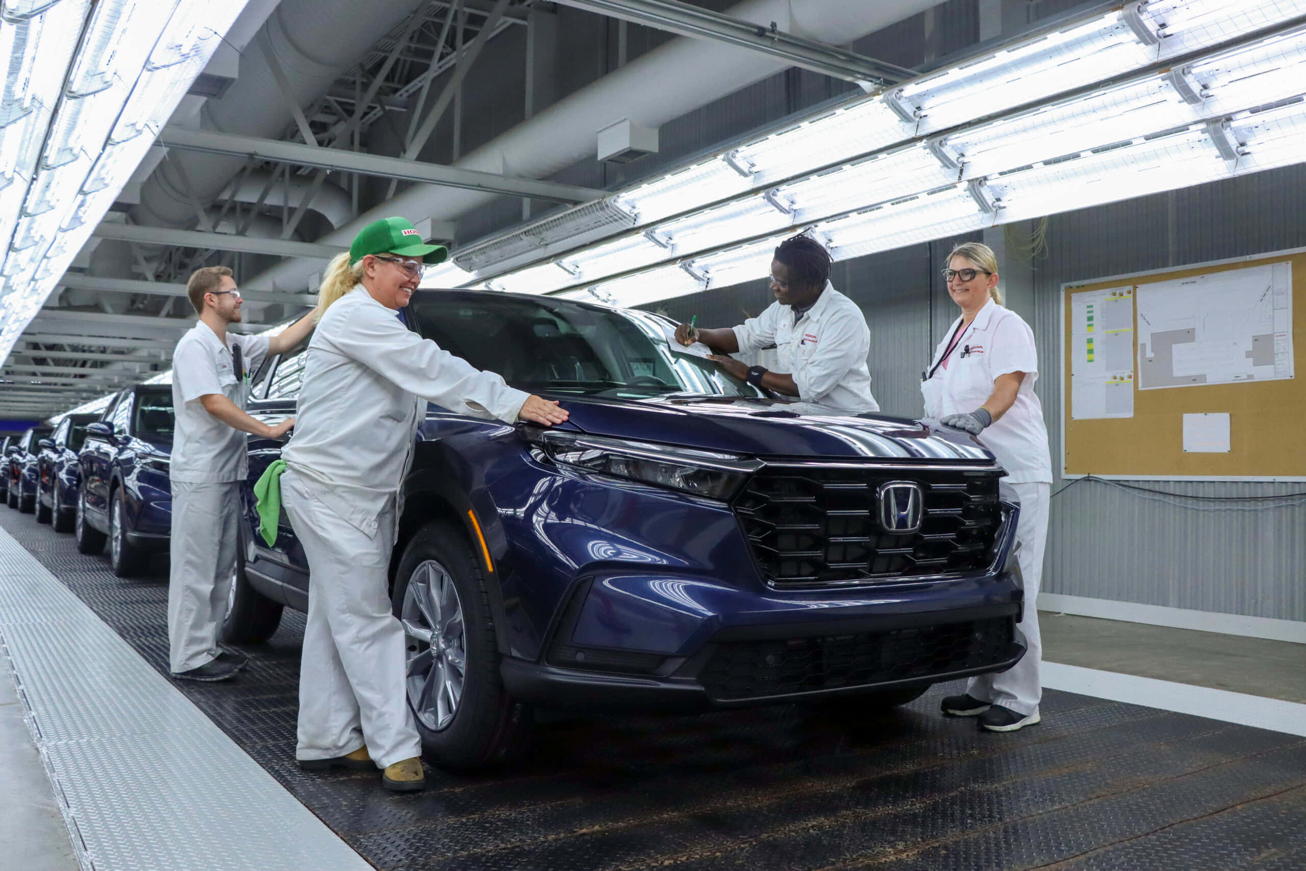 Honda Cr-v 桌布 壁紙 — 身穿白色制服嘅工廠工人喺明亮嘅螢光燈下檢查裝配線上嘅光面藍色本田SUV。