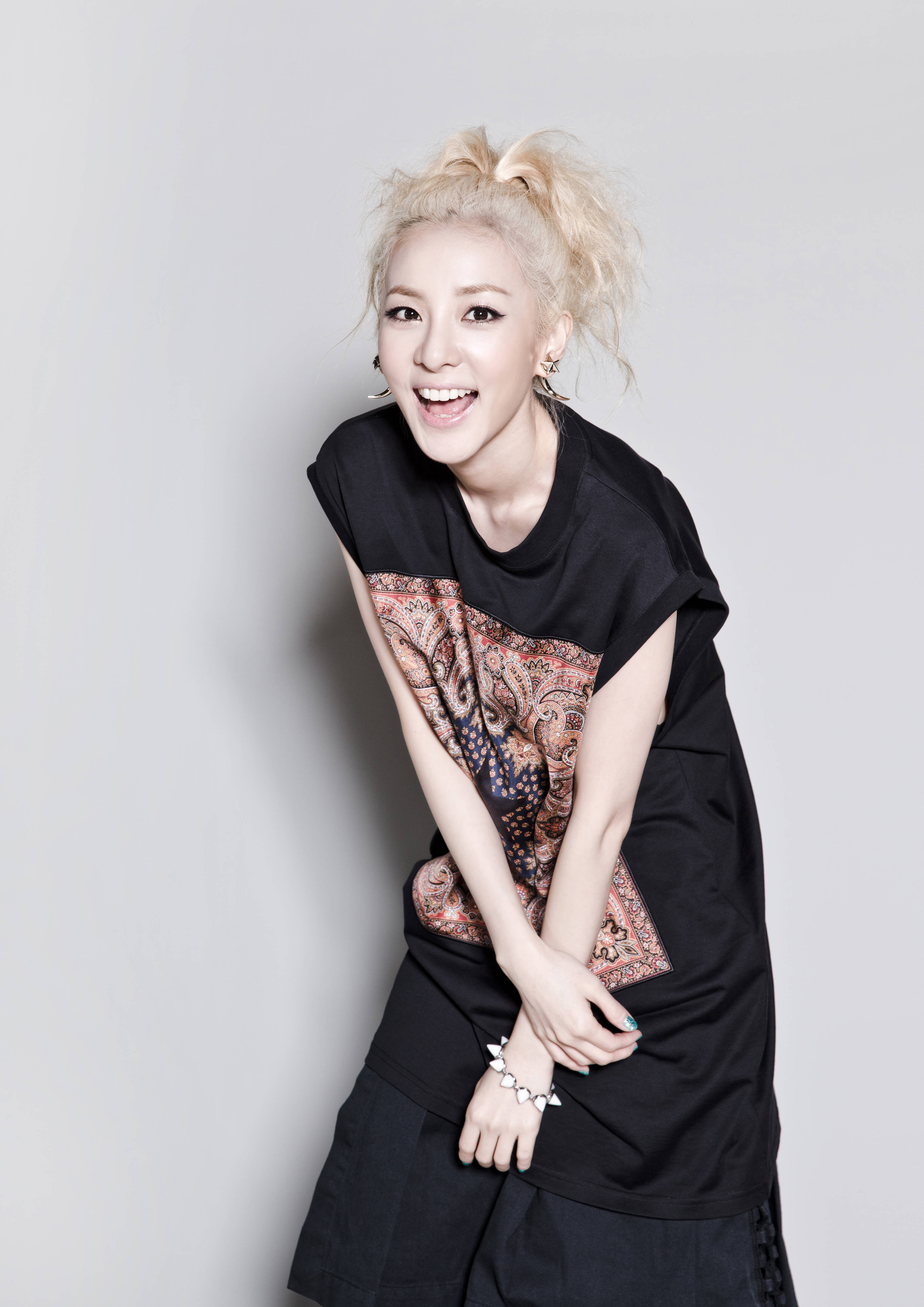 Sandara 2NE1 美拍 壁紙 — 一位快樂的金髮女性，頭髮亂糟糟地紮成髮髻，穿著帶有佩斯利圖案的黑色T恤，開懷大笑。