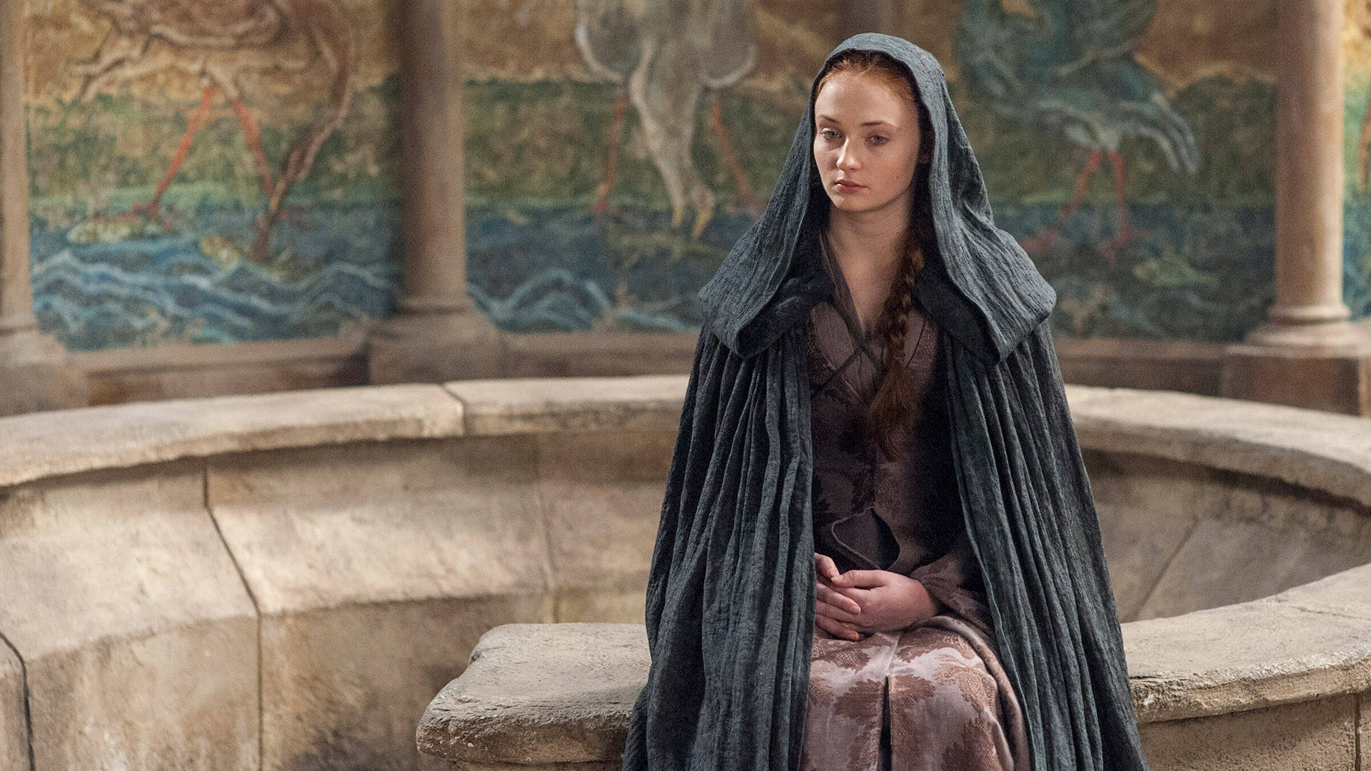 Sansa Stark《冰與火之歌》 壁紙 — 一位身穿深色連帽斗篷的年輕女子莊嚴地坐在石凳上，身後是帶有彩繪壁畫的古老柱子。