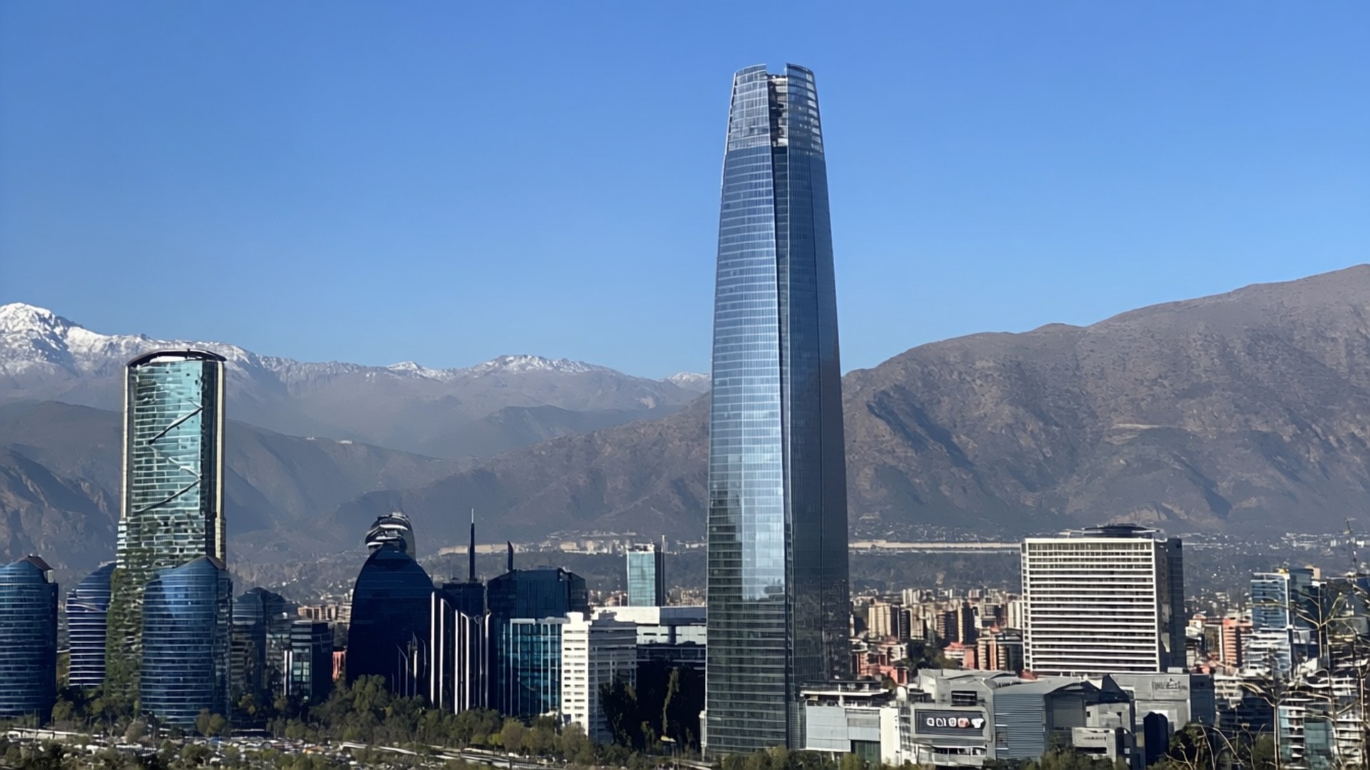 現代玻璃摩天大樓聳立於城市之上，遠處有白雪覆蓋的山峰。