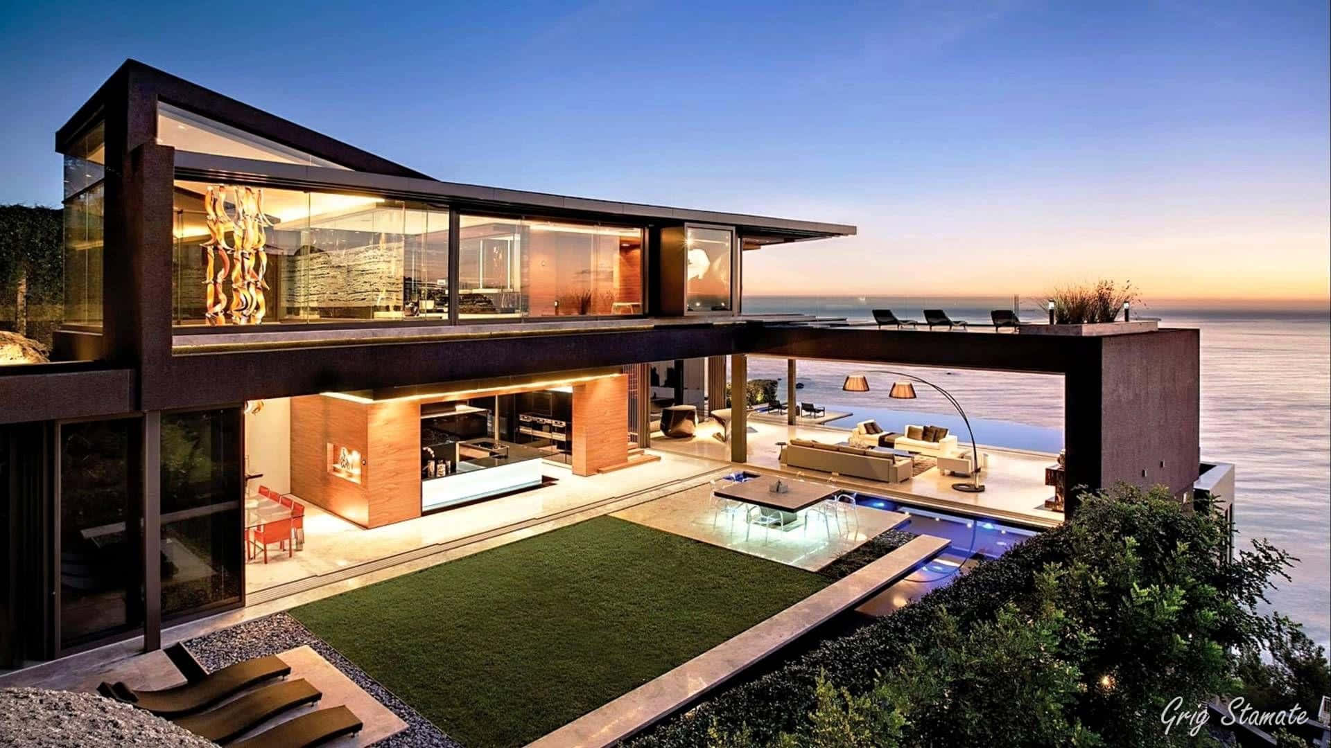 SAOTA Homes 設計的海濱豪宅 壁紙 — 現代玻璃屋坐落在懸崖上，俯瞰黃昏時分的海洋，內部發光，下方有游泳池。