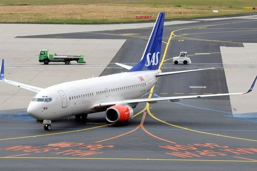 SAS飛機在機場停機坪上，有地面車輛和塗漆標記。