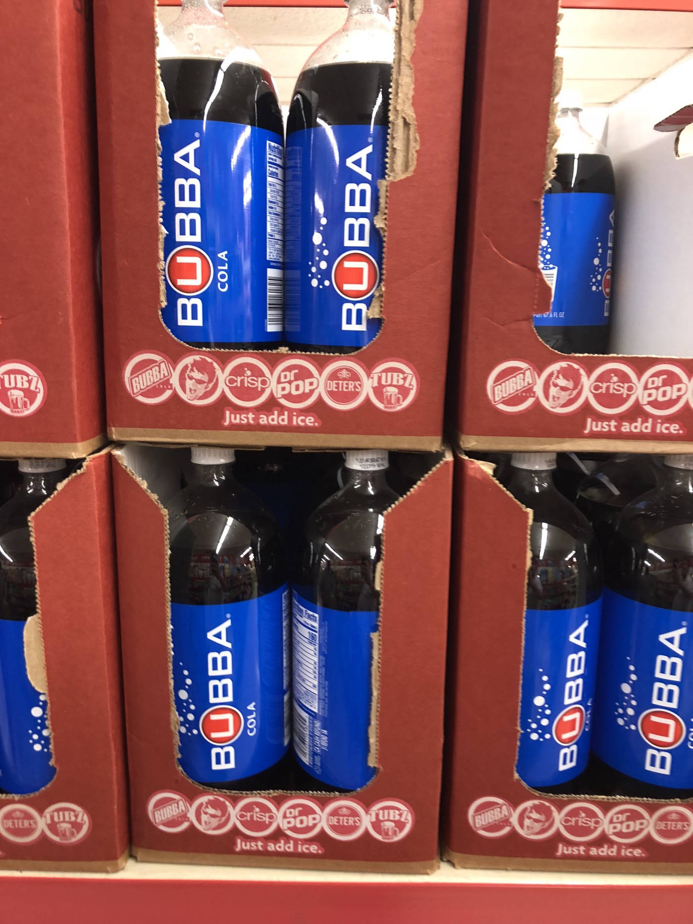 Save A Lot 超市 Bubba Cola 壁紙 — 一排排Bubba Cola瓶裝在紅色紙箱中，上面印有'Just add ice'標語，陳列在商店走道。