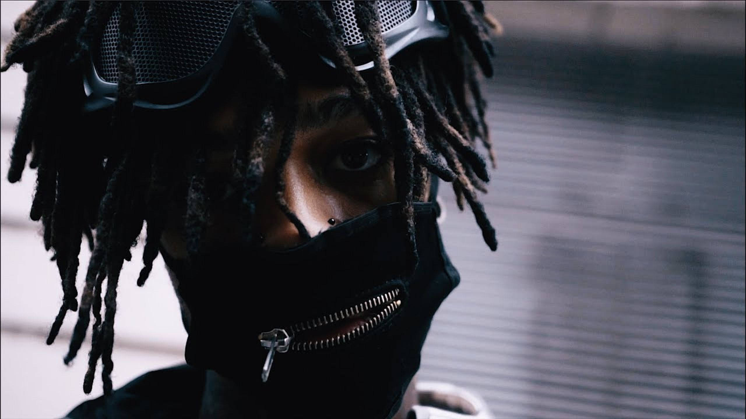 Scarlxrd 憤怒氣息 壁紙 — 一個留著辮子、戴著黑色拉鍊面罩的人，透過模糊的城市背景凝視著。