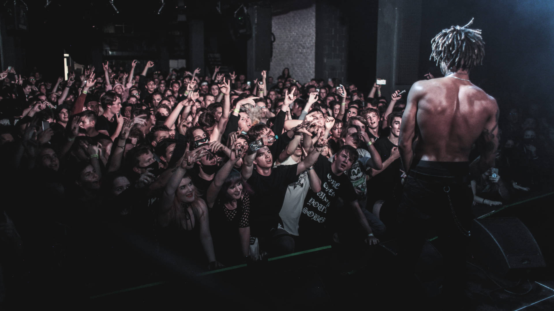 Scarlxrd 深層地下演唱會現場 壁紙 — 一位赤膊的雷鬼辮音樂家在舞台上表演，背光聚光燈照射，充滿活力的觀眾興奮地舉起雙手。