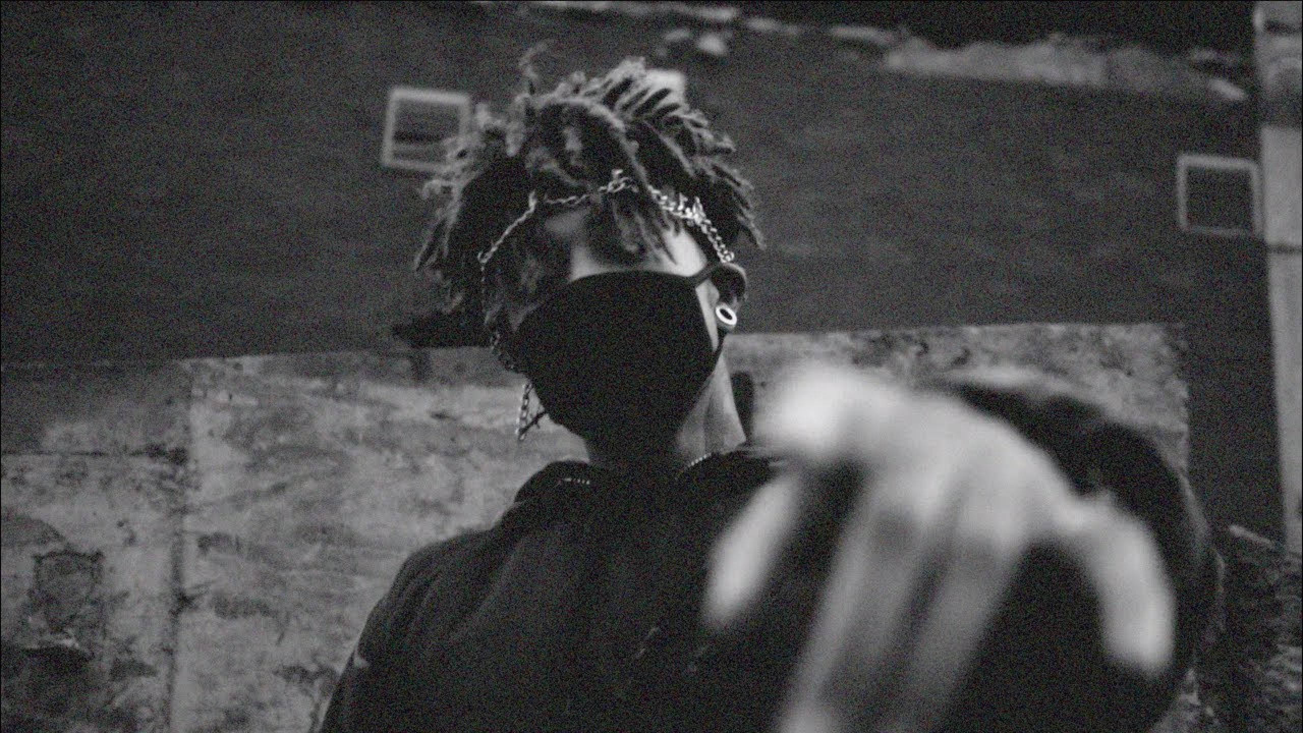 Scarlxrd 粒狀效果 壁紙 — 一個留著辮子頭、戴著口罩的人，在粗糙的城市牆壁背景下，向觀眾伸出一隻模糊的手。
