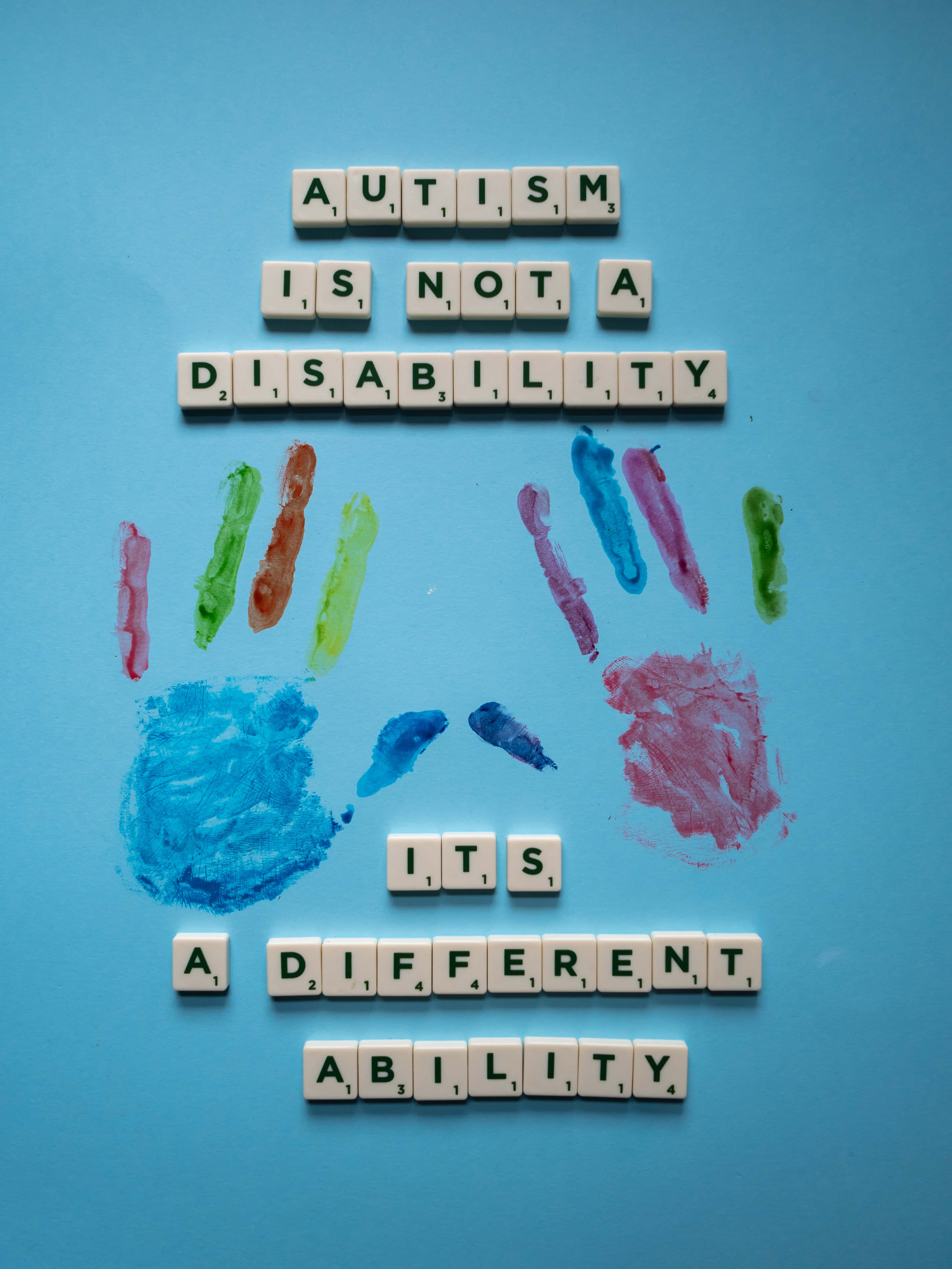 Autism 桌布 壁紙 — Scrabble 字母磚在藍色背景上的彩色手印上方拼出「自閉症不是殘疾，而是一種不同的能力」。