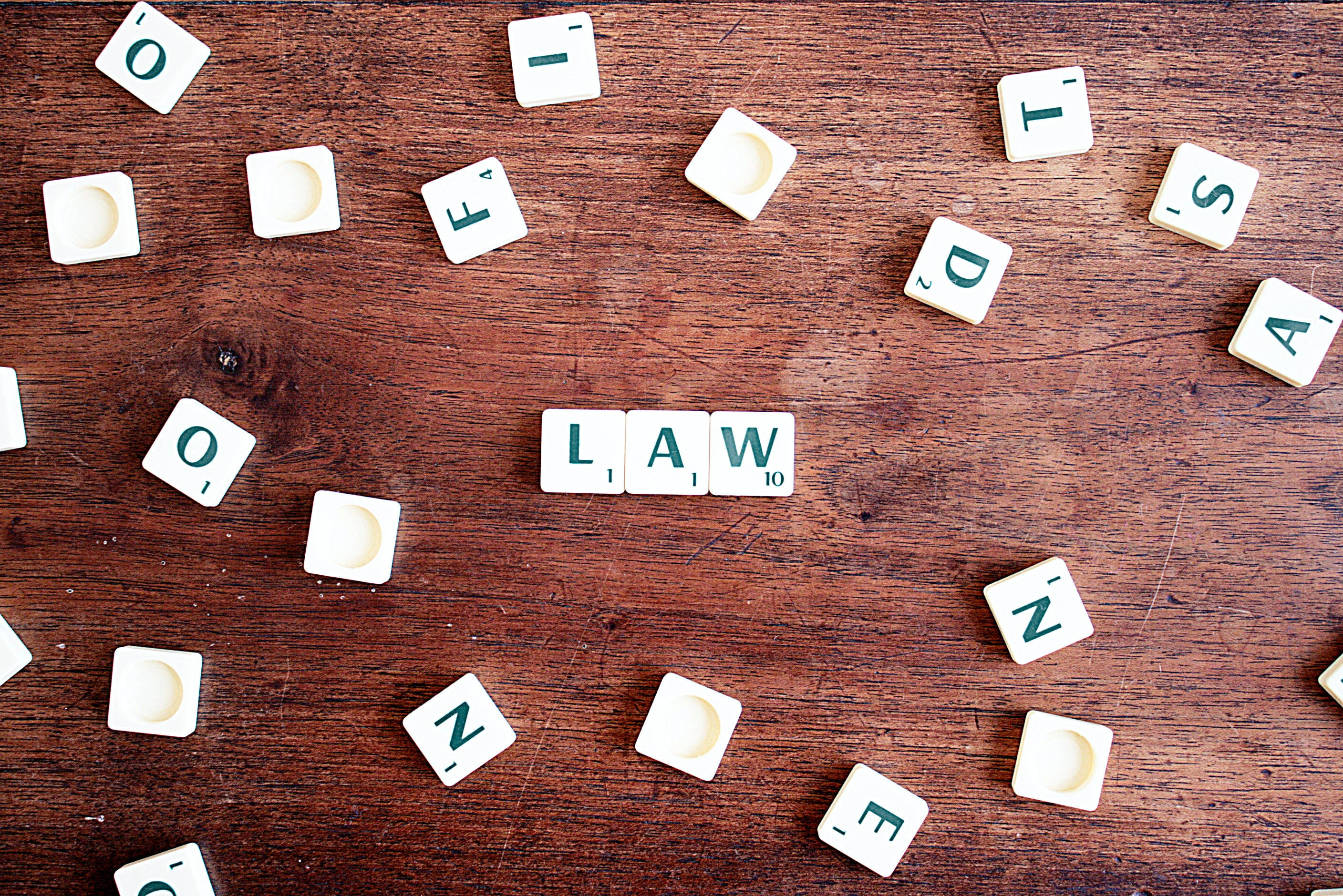 Scrabble 字母磚在木質表面上拼出 law 字樣，周圍散落著空白字母磚。