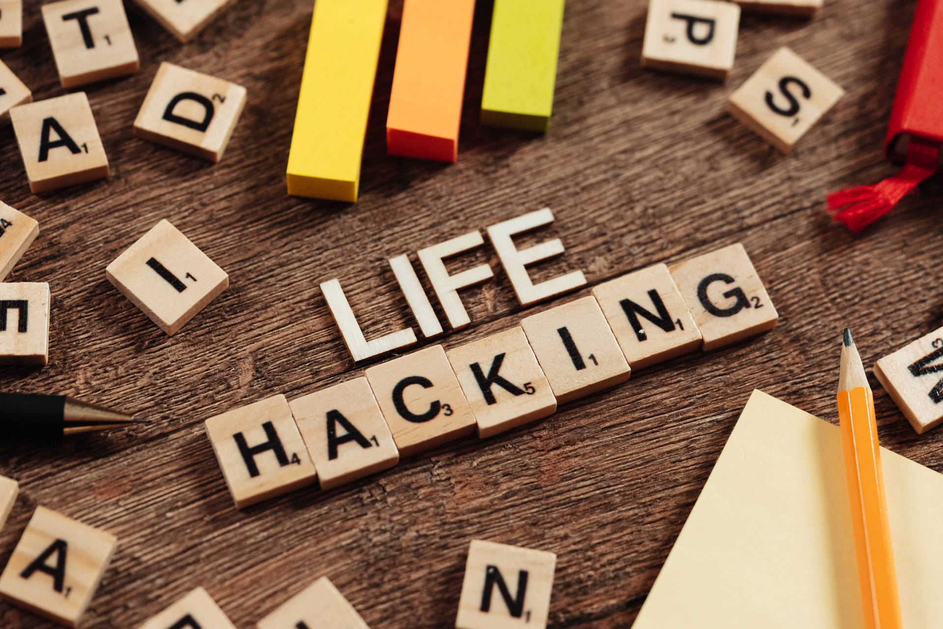 Scrabble 字母磚在木桌上拼出 life hacking，旁邊有彩色積木和鉛筆。