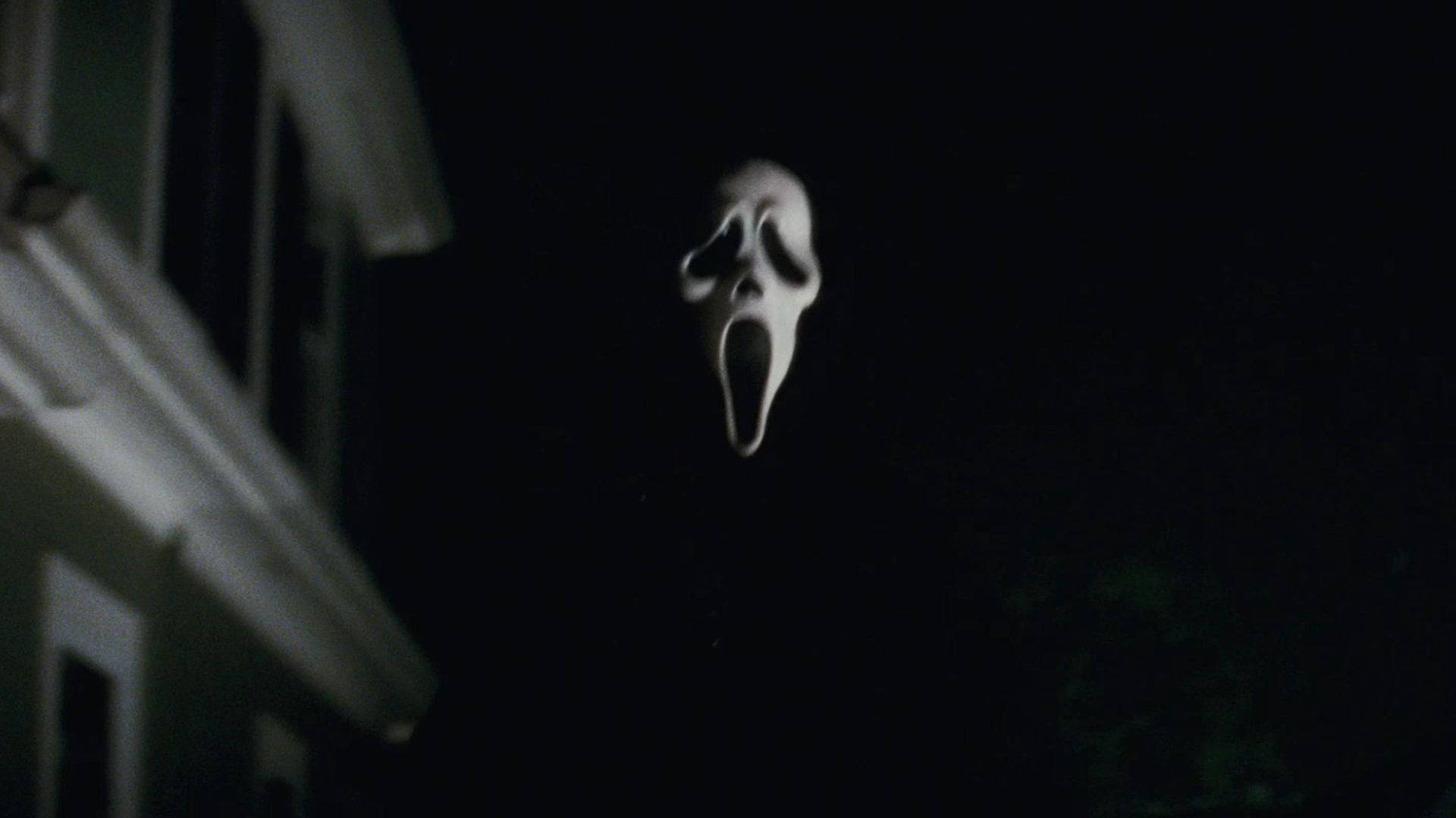 《Scream》Ghostface 驚悚面具 壁紙 — 一個發光的白色鬼面具在夜晚陰森地懸浮在一間黑暗的房子前。