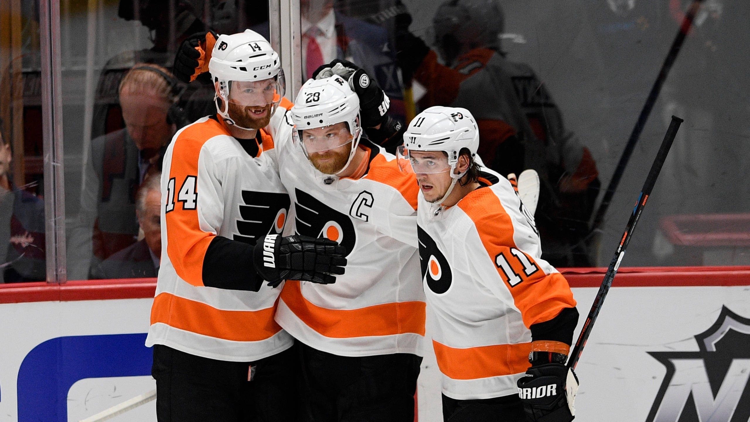 Sean Couturier 獲勝慶祝 壁紙 — 三名身穿白色和橙色球衣的費城飛人冰球球員在冰上慶祝入球，表情激動。
