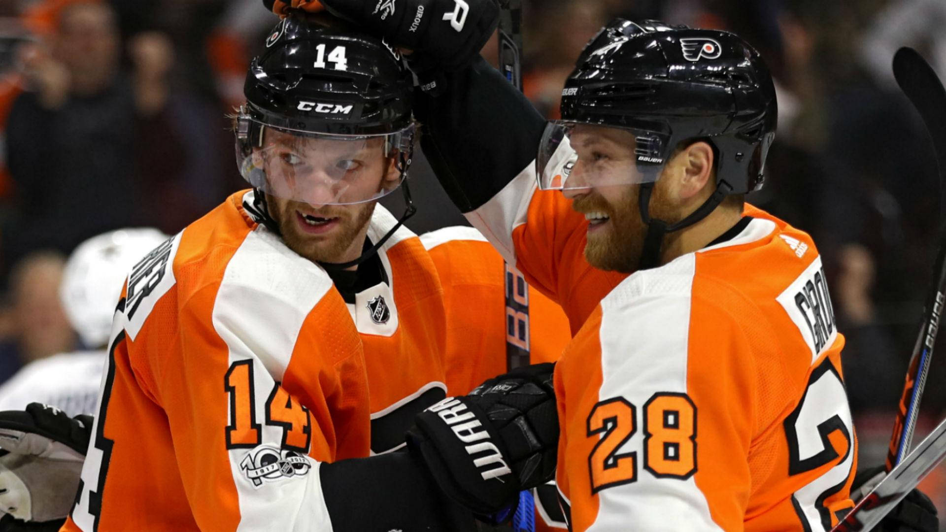 Sean Couturier 與隊友 壁紙 — 兩名身穿橙色和白色球衣的費城飛人冰球運動員，以強烈的表情和舉起的球棍慶祝入球。