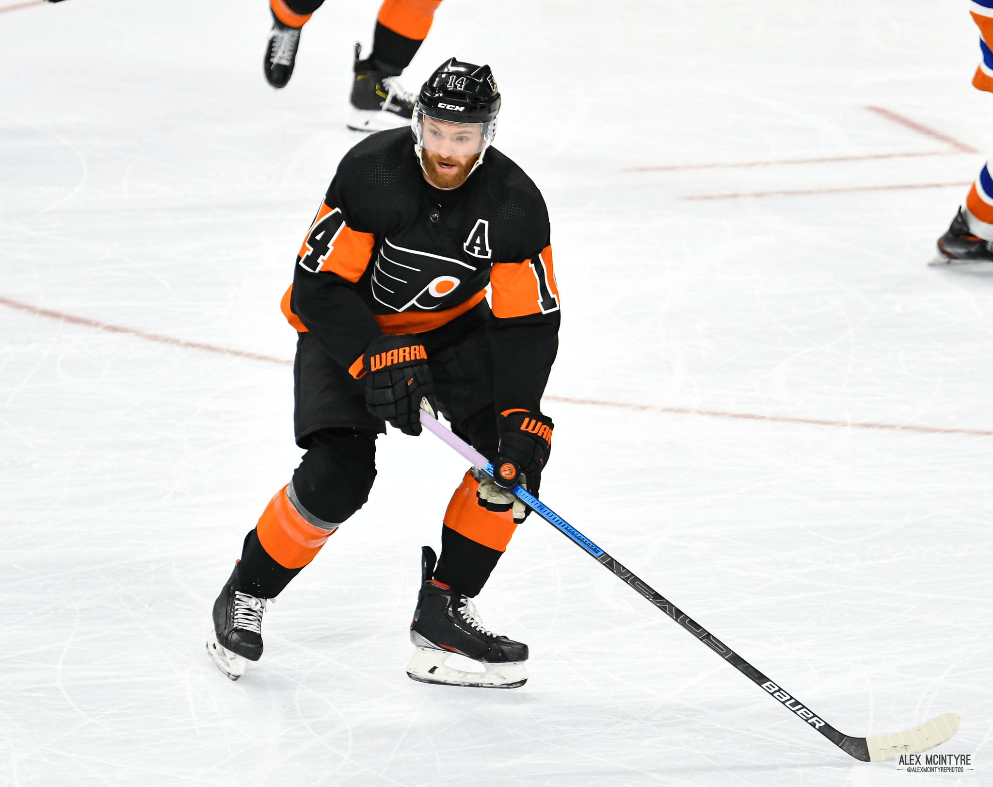 Sean Couturier 著黑橙戰袍 壁紙 — 一名身穿黑色和橙色裝備的冰球運動員在冰上專注地激烈滑行。
