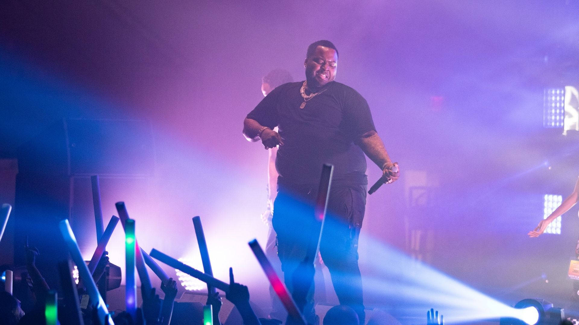 Sean Kingston 活力舞蹈 壁紙 — 一位男性表演者在充滿活力的紫色和藍色舞台燈光下，用發光的螢光棒為人群注入活力。