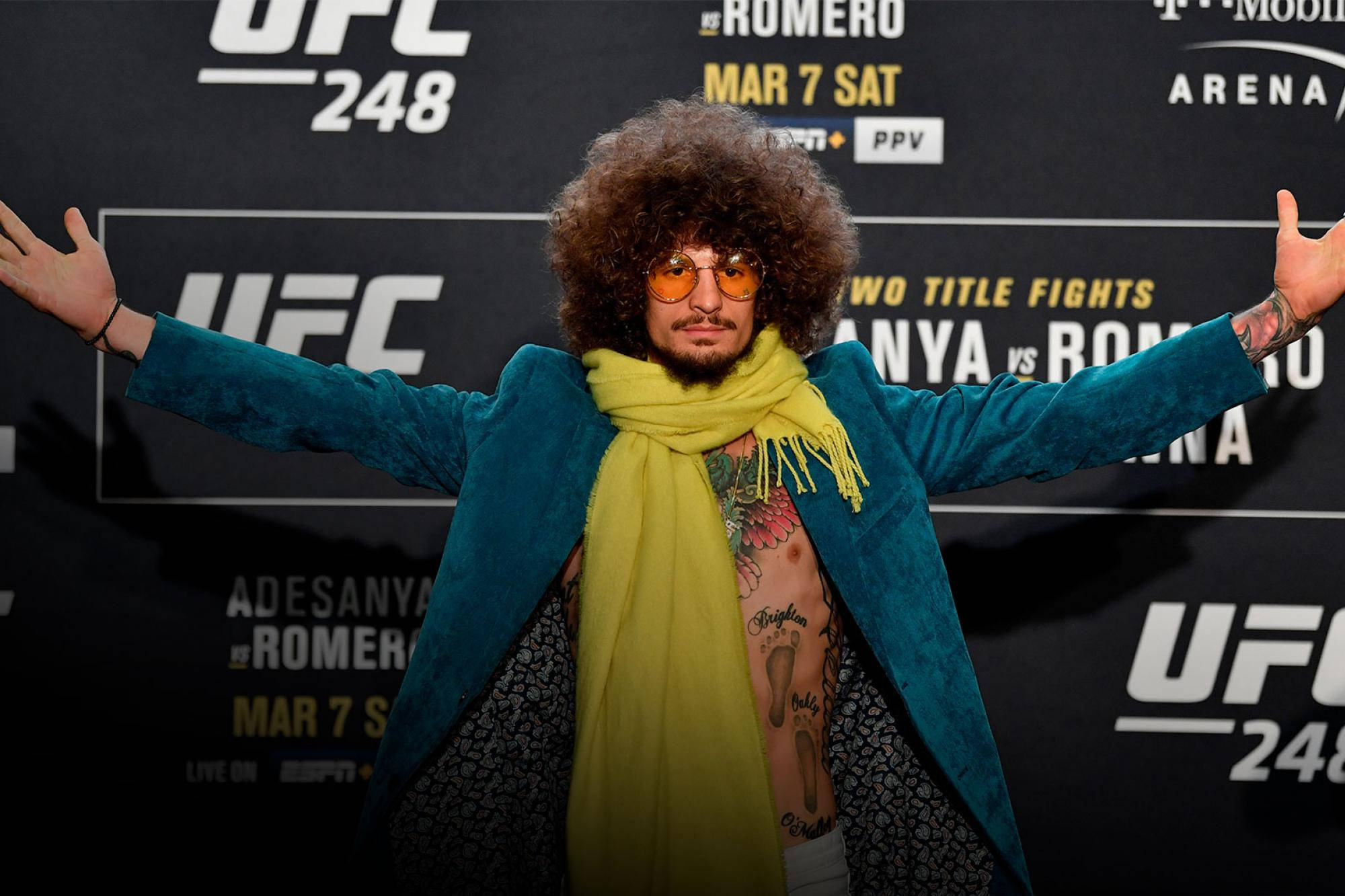 UFC活動中留爆炸頭戴太陽眼鏡的男人，身穿藍綠色外套和黃色圍巾。