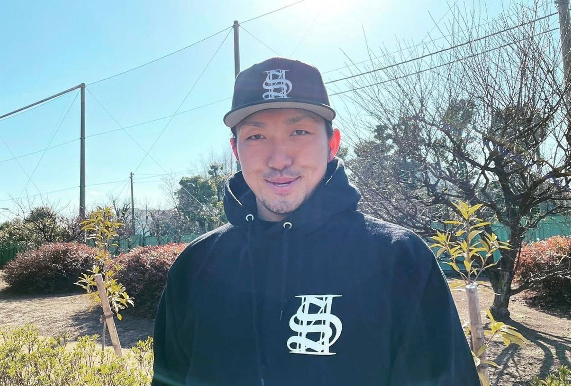 男人穿著黑色連帽衫和帽子在陽光明媚的日子裡微笑著在戶外。