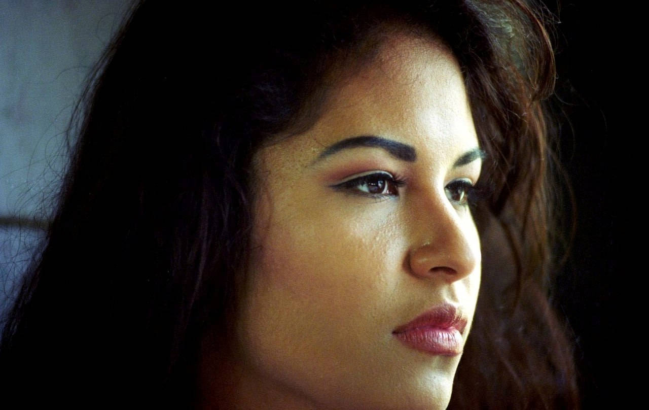 Selena Quintanilla 近照 壁紙 — 一個特寫肖像，一位深色頭髮、眼神銳利的女性在深色背景下若有所思地望向一旁。