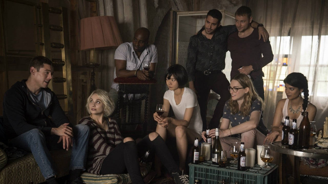 《Sense8》不滅之隊 壁紙 — 七個人聚集在燈光昏暗的復古房間裡，圍著一箱瓶子分享飲料和交談。