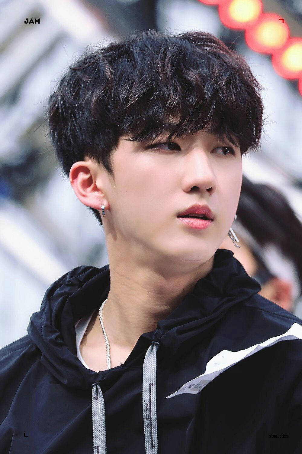 Seo Changbin 隨拍照 壁紙 — 一位擁有深色捲髮和銀色耳環的年輕男子，穿著帶有白色點綴的黑色連帽衫，若有所思地凝視著。