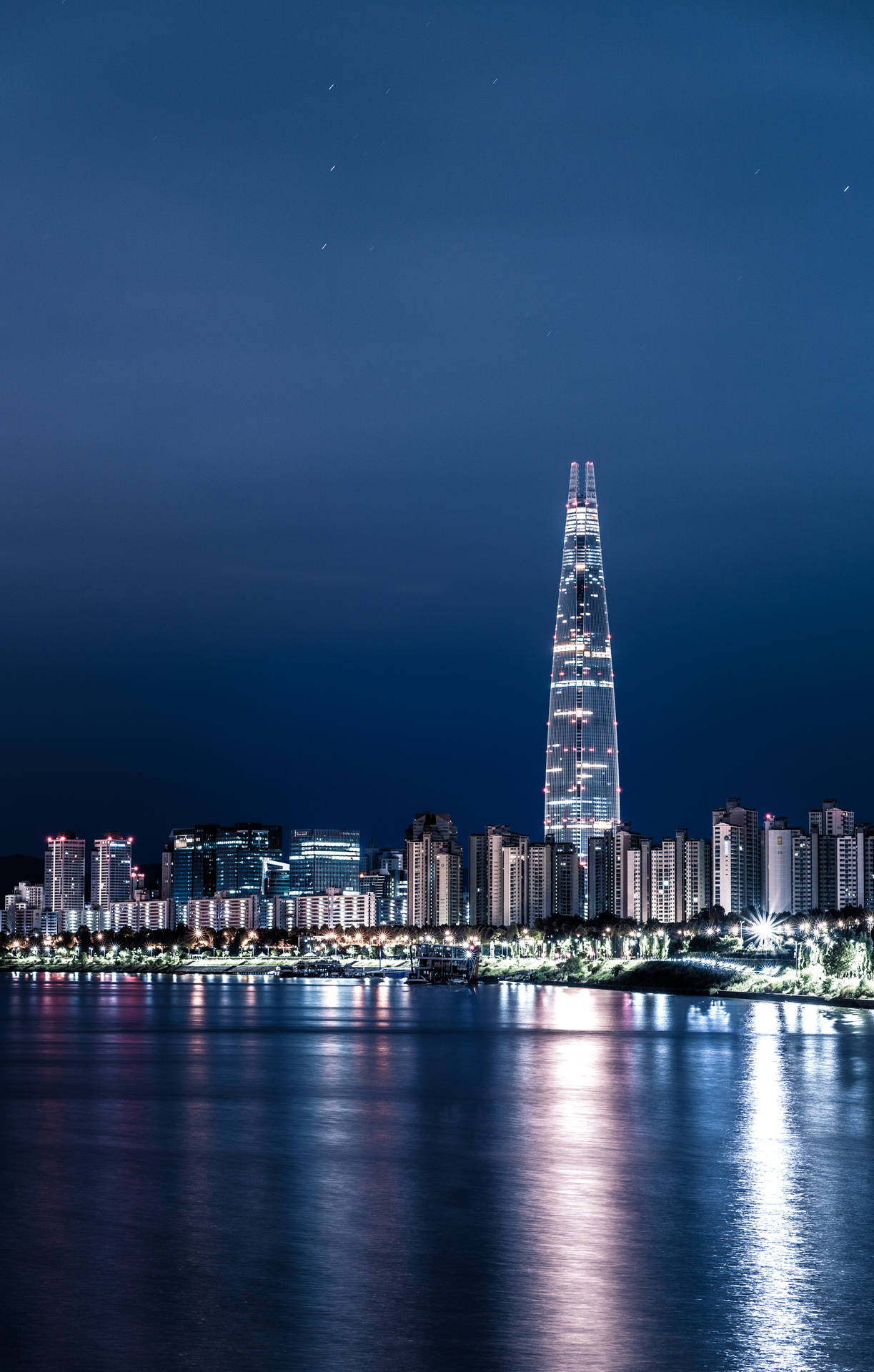 星空下，燈光璀璨的摩天大樓倒映在水面上的夜景